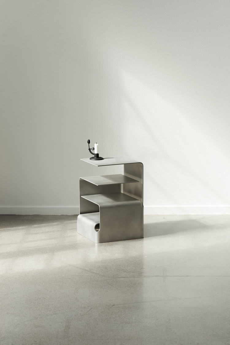 Unika Auction by Bjørn van den Berg and Falke Svatun — A shelving unit with three staggered horizontal planes in brushed stainless steel, formed into an organic S-shaped curved profile.