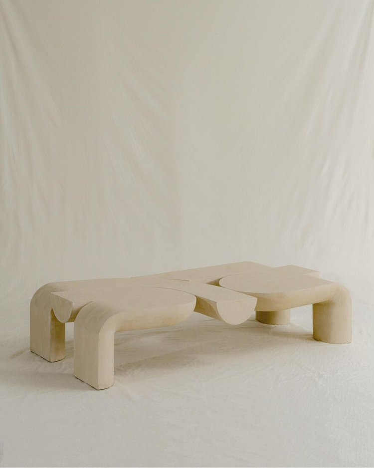 Kosa Collection by Ian Felton — A sculptural bench in light timber showcases organic, rounded forms with tubular armrests that curve upward in continuous loops.