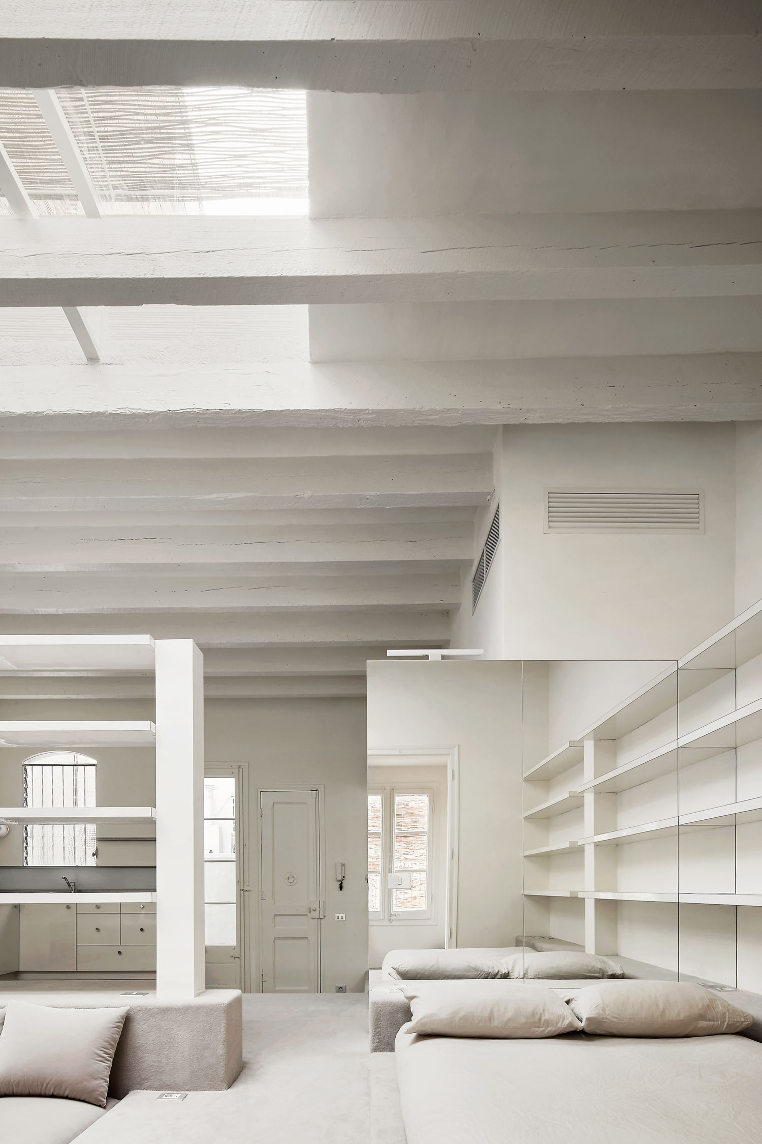 Barcelona Apartment Renovation by Arquitectura-G — A sunken lounge occupies the lower level of this Barcelona loft, its white upholstered seating arranged on pale-grey carpeting that unifies the stepped zones.