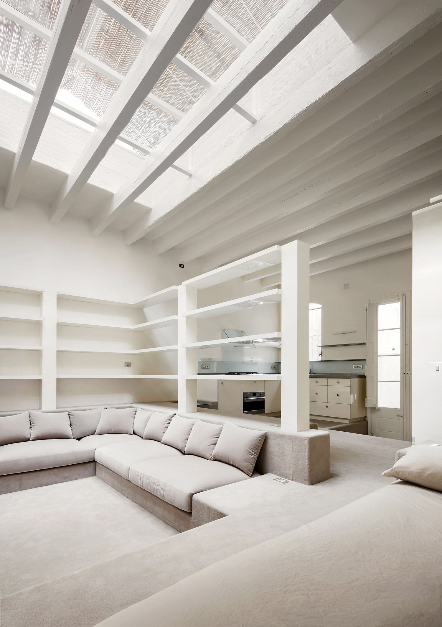 Barcelona Apartment Renovation by Arquitectura-G — A sunken seating area anchors the open-plan Barcelona apartment, its white linen upholstery and grey carpet establishing a lower visual plane.