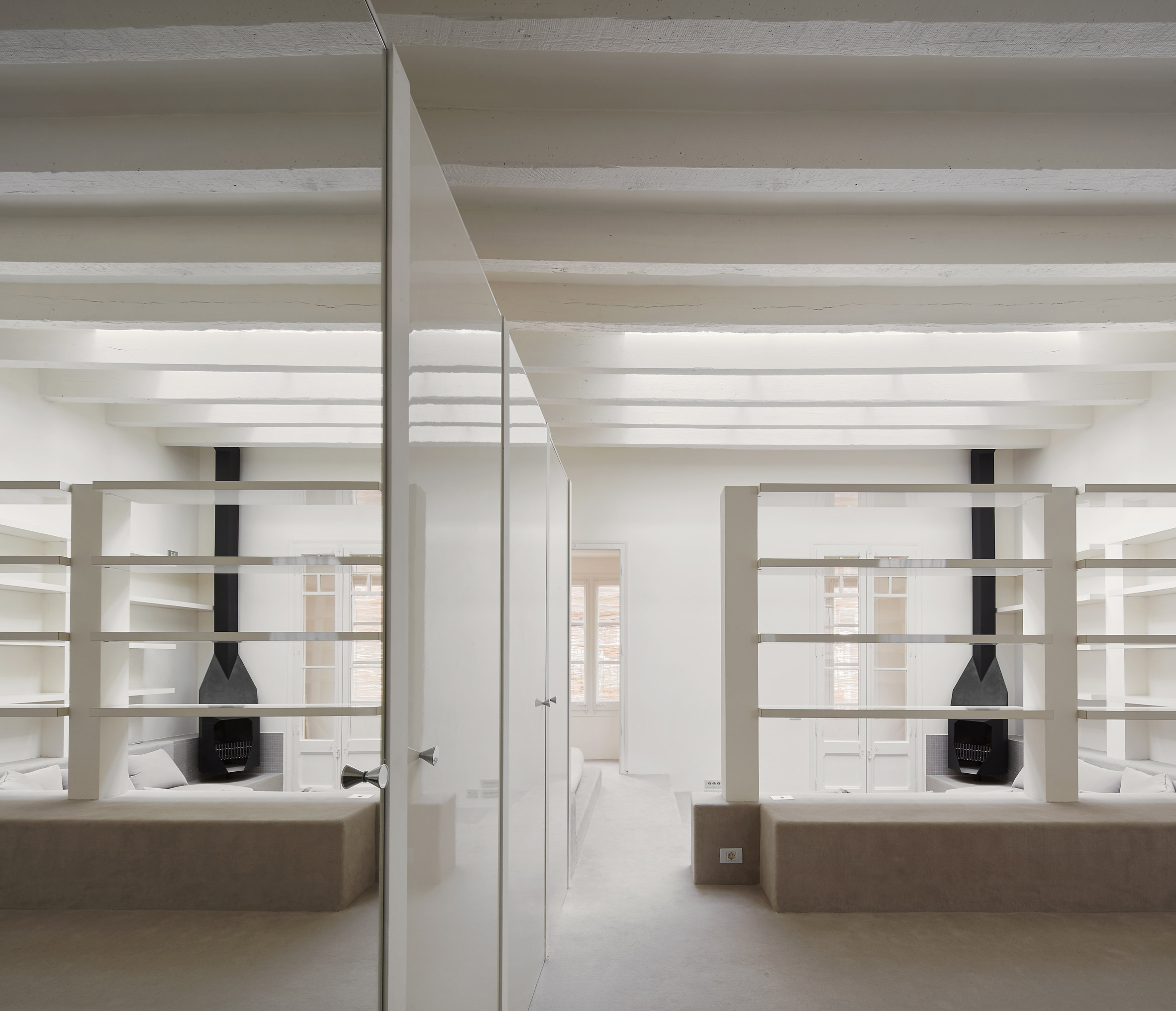 Barcelona Apartment Renovation by Arquitectura-G — A mirrored perspective of the Barcelona apartment's dual living zones, separated by a central glass partition.