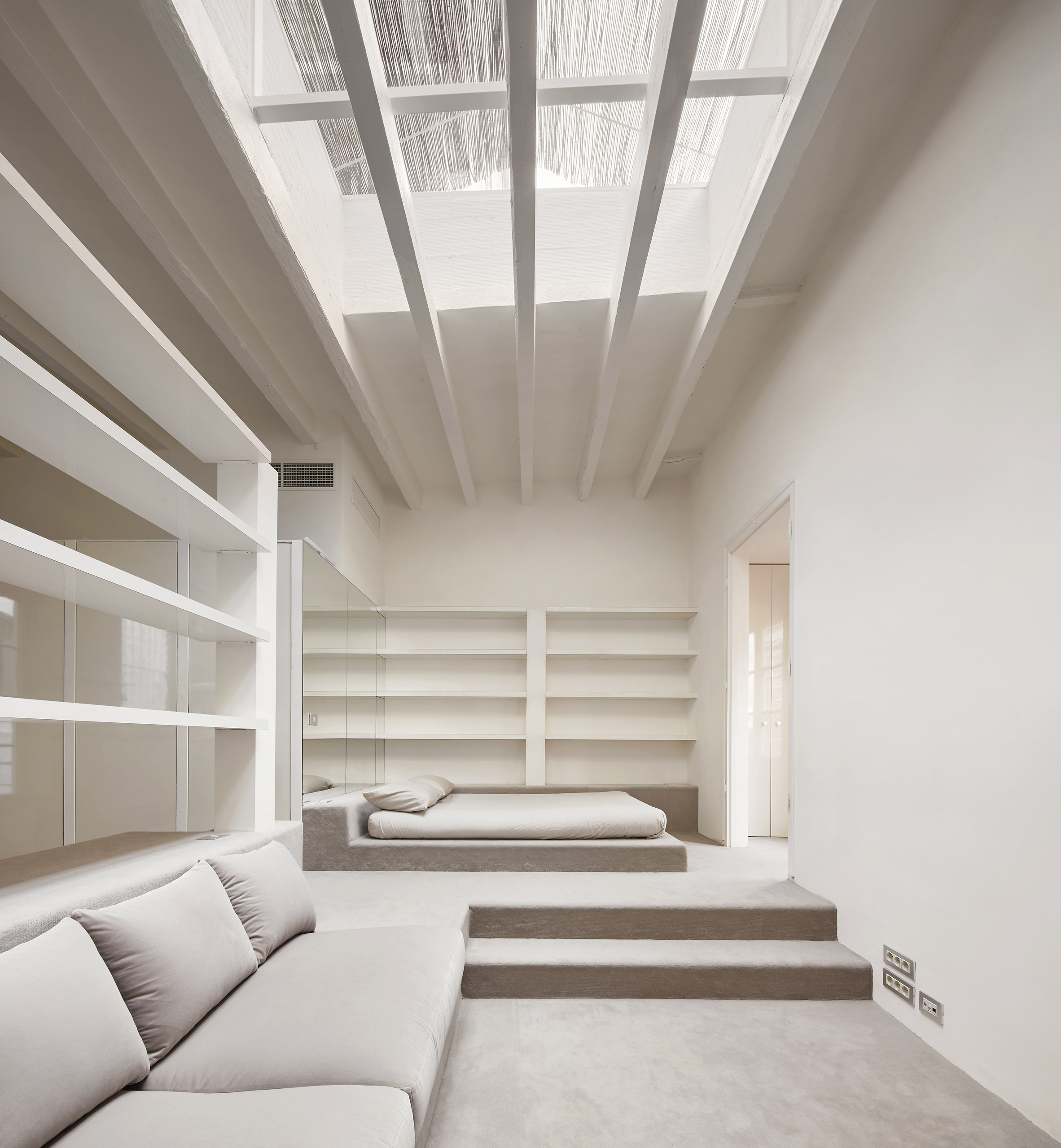 Barcelona Apartment Renovation by Arquitectura-G — A sunken lounge occupies the lower level of this Barcelona apartment, its white upholstered seating positioned beneath a dramatic gridded skylight.