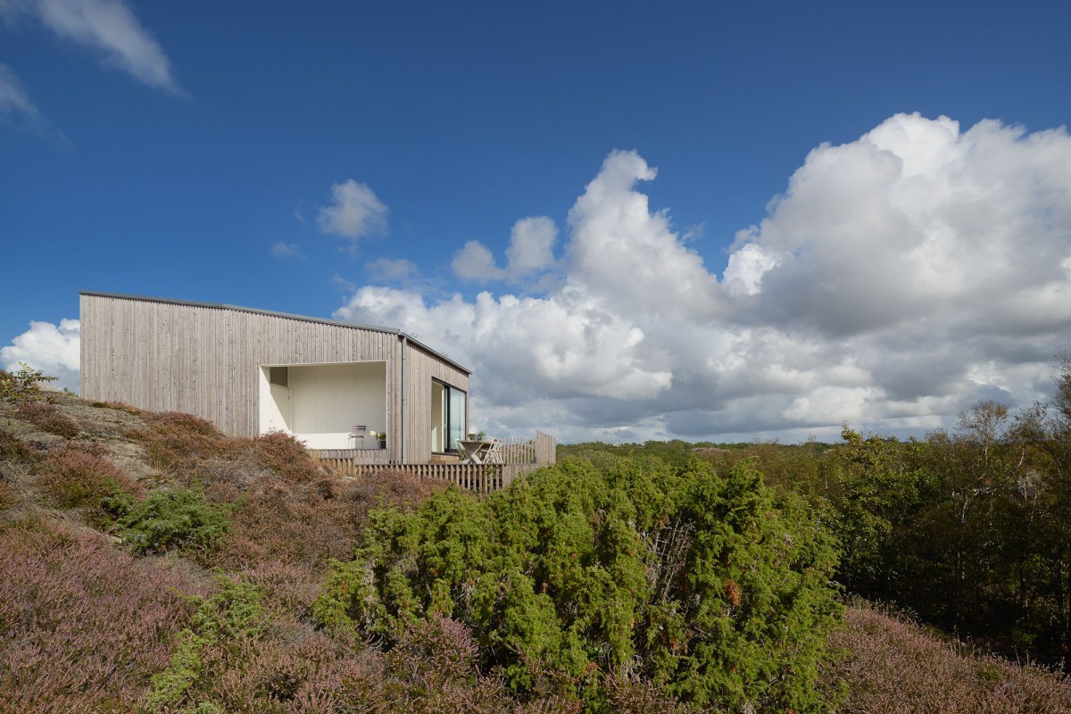 Kyrkesund Weekend House by Mattias Gunneflo — A corrugated metal-clad weekend house sits elevated on the rocky Scandinavian landscape, its horizontal form anchored by slender supports that create visual...