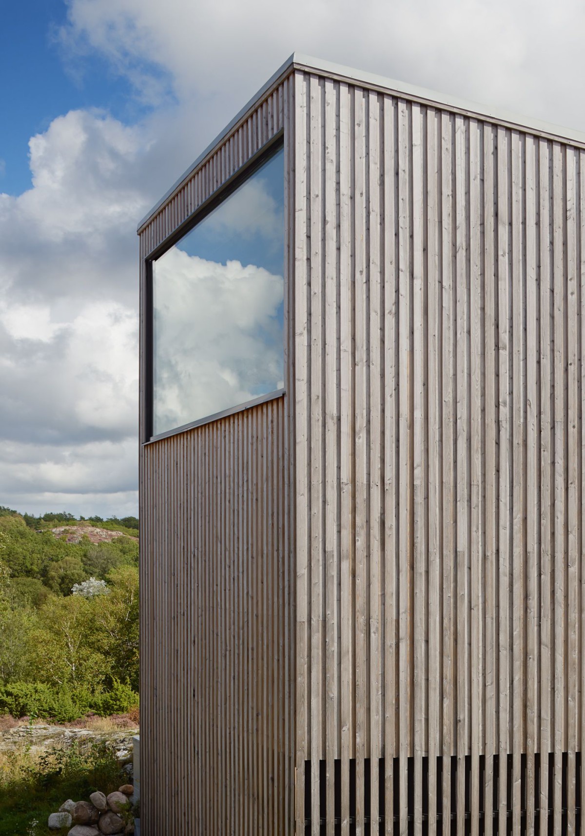 Kyrkesund Weekend House by Mattias Gunneflo — A corrugated steel facade with weathered patina dominates the frame, its vertical ribbing interrupted by a horizontal ribbon window positioned at mid-height.