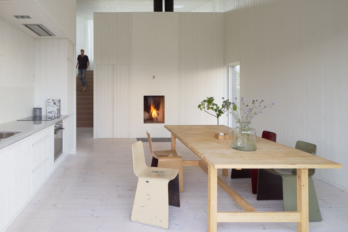 Kyrkesund Weekend House by Mattias Gunneflo — The Kyrkesund Weekend House interior reveals a spare, light-filled living space anchored by a substantial timber dining table with exposed joinery.