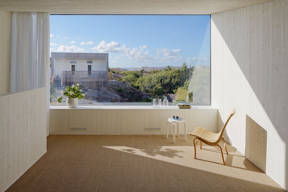 Kyrkesund Weekend House by Mattias Gunneflo — A sunlit interior space frames the Scandinavian landscape through a continuous horizontal window.