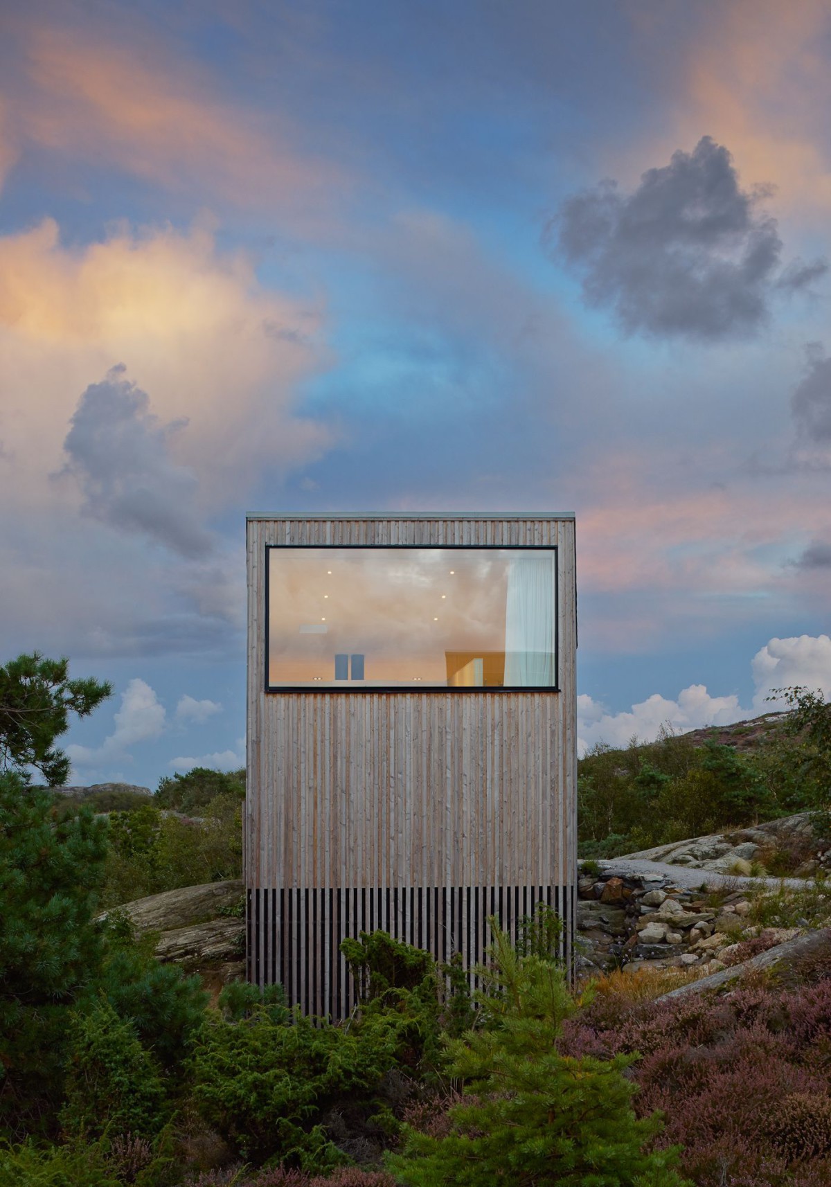 Kyrkesund Weekend House by Mattias Gunneflo — A corrugated metal-clad weekend house elevated on slender vertical supports sits isolated within rocky Scandinavian terrain.