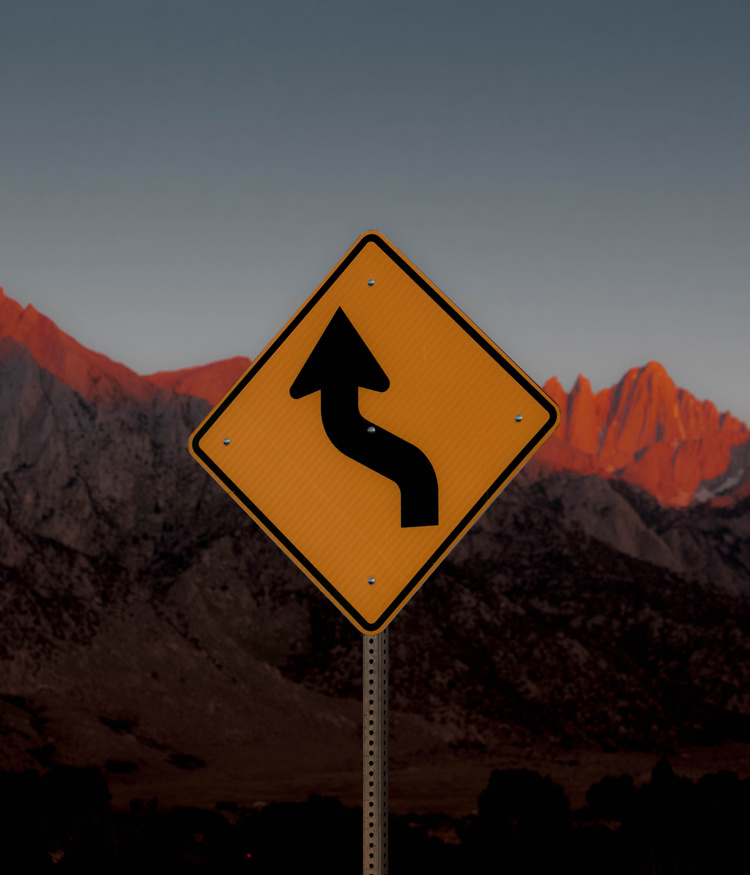 Selected works by Leeor Wild — A diamond-shaped yellow warning sign dominates the composition, mounted on a metal post against a desert landscape.