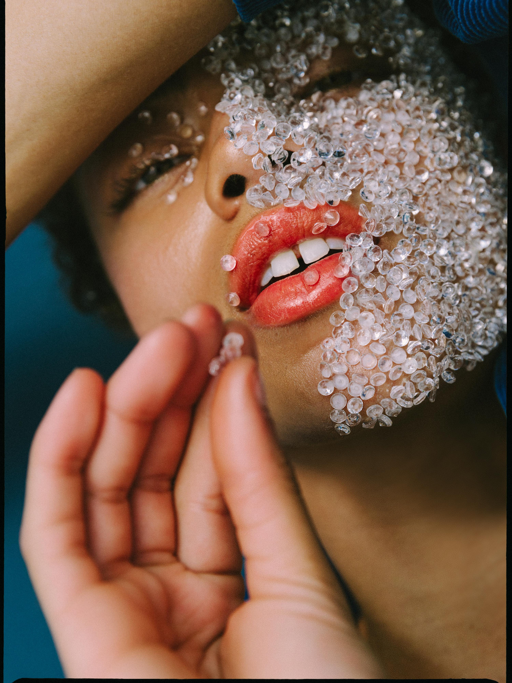 Selected works by Leeor Wild — Close-up portrait photograph capturing a face partially obscured by translucent beaded material in clear and frosted tones.