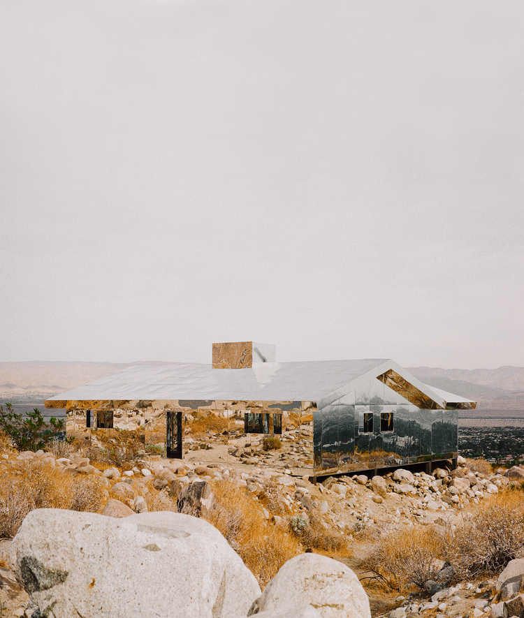Selected works by Leeor Wild — Two mirrored pavilion structures with inverted pitched-roof forms occupy a boulder-strewn desert plateau.