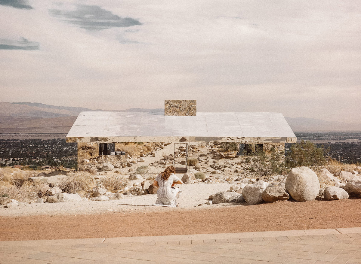 Selected works by Leeor Wild — A mirrored pavilion structure anchors a rocky desert landscape, its white roof plane reflecting the pale sky while dark timber framing remains visible...