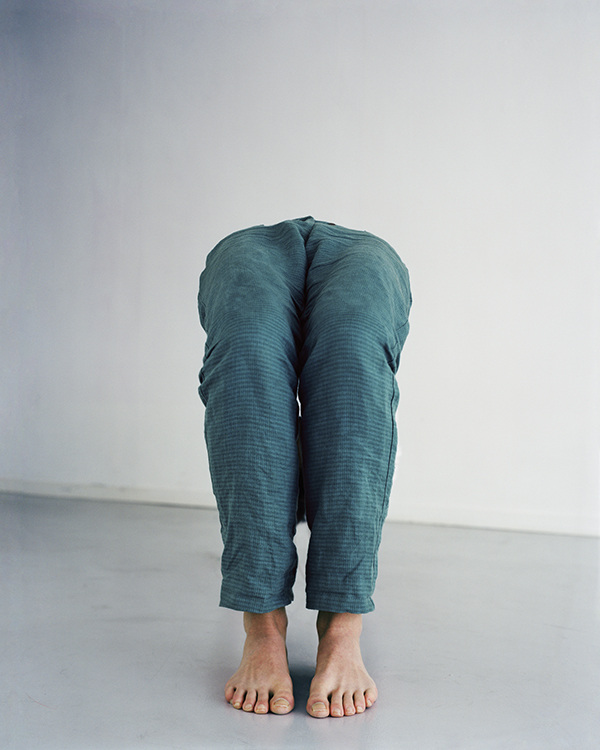 The Circle and the Line by Erik Östensson — A figure stands barefoot against a neutral ground, legs and torso enveloped in crumpled teal linen fabric that obscures the body's contours.