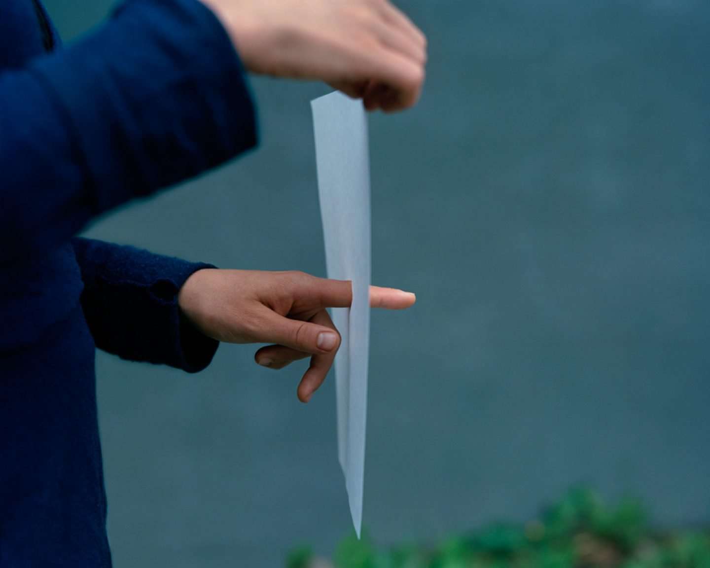 The Circle and the Line by Erik Östensson — Two hands manipulate a rectangular sheet of white paper or fabric against a teal background, rendering the material taut and planar.