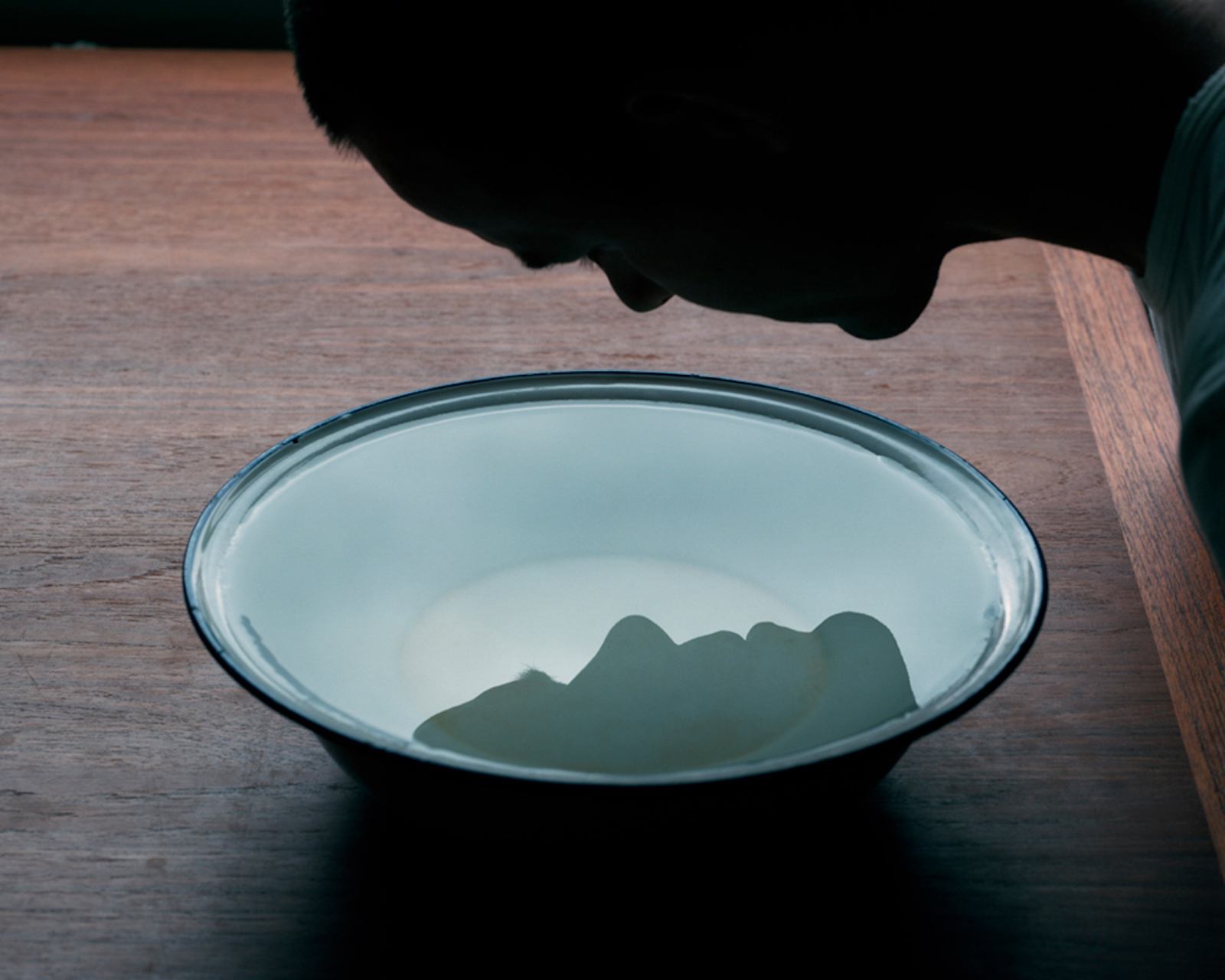 The Circle and the Line by Erik Östensson — A ceramic bowl containing clear water sits on a wooden surface alongside dark fabric.