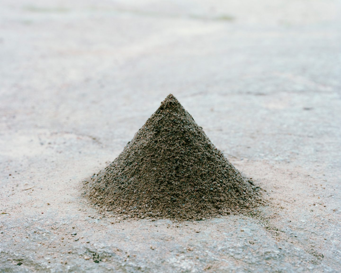The Circle and the Line by Erik Östensson — A conical mound of sand or fine aggregate rises from a flat ground plane, its apex sharply defined against a diffused sky.