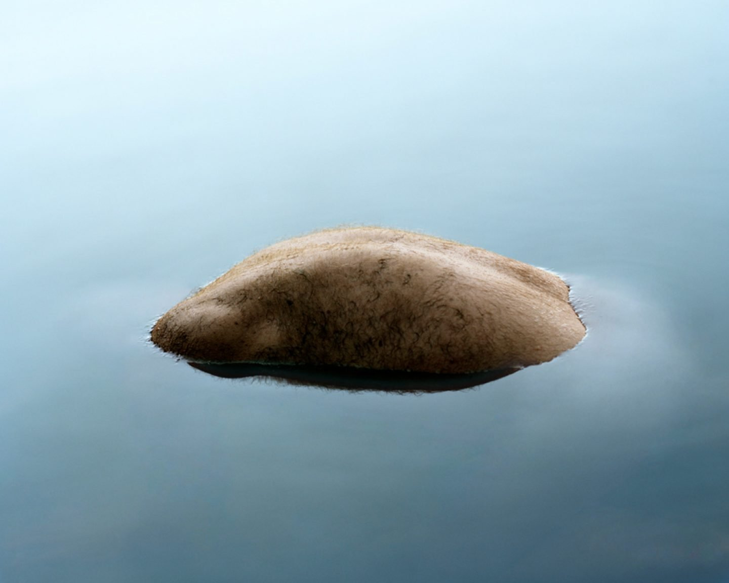 The Circle and the Line by Erik Östensson — A human form lies beneath white fabric against a grey-blue sky, creating a sculptural mound.