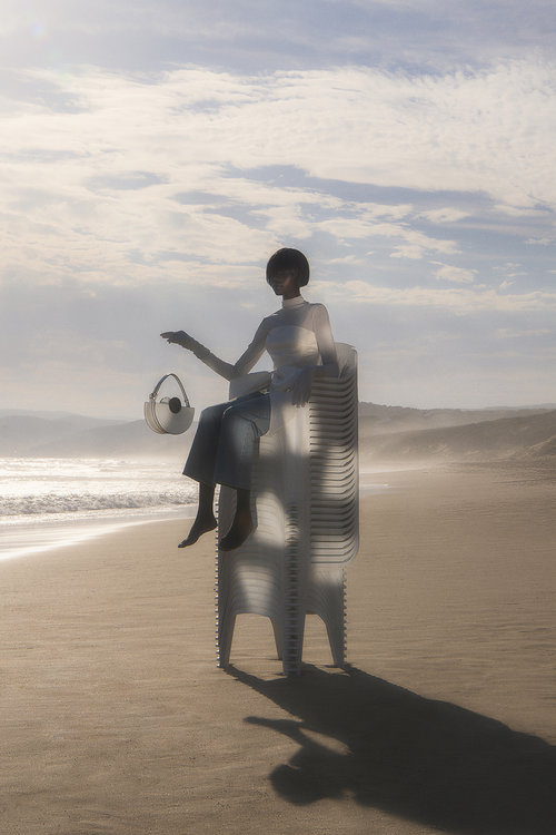 Selected works by Abdulla Elmaz — A figure sits atop a monolithic fiberglass sculpture ribbed with vertical striations, positioned on a Dubai beach.