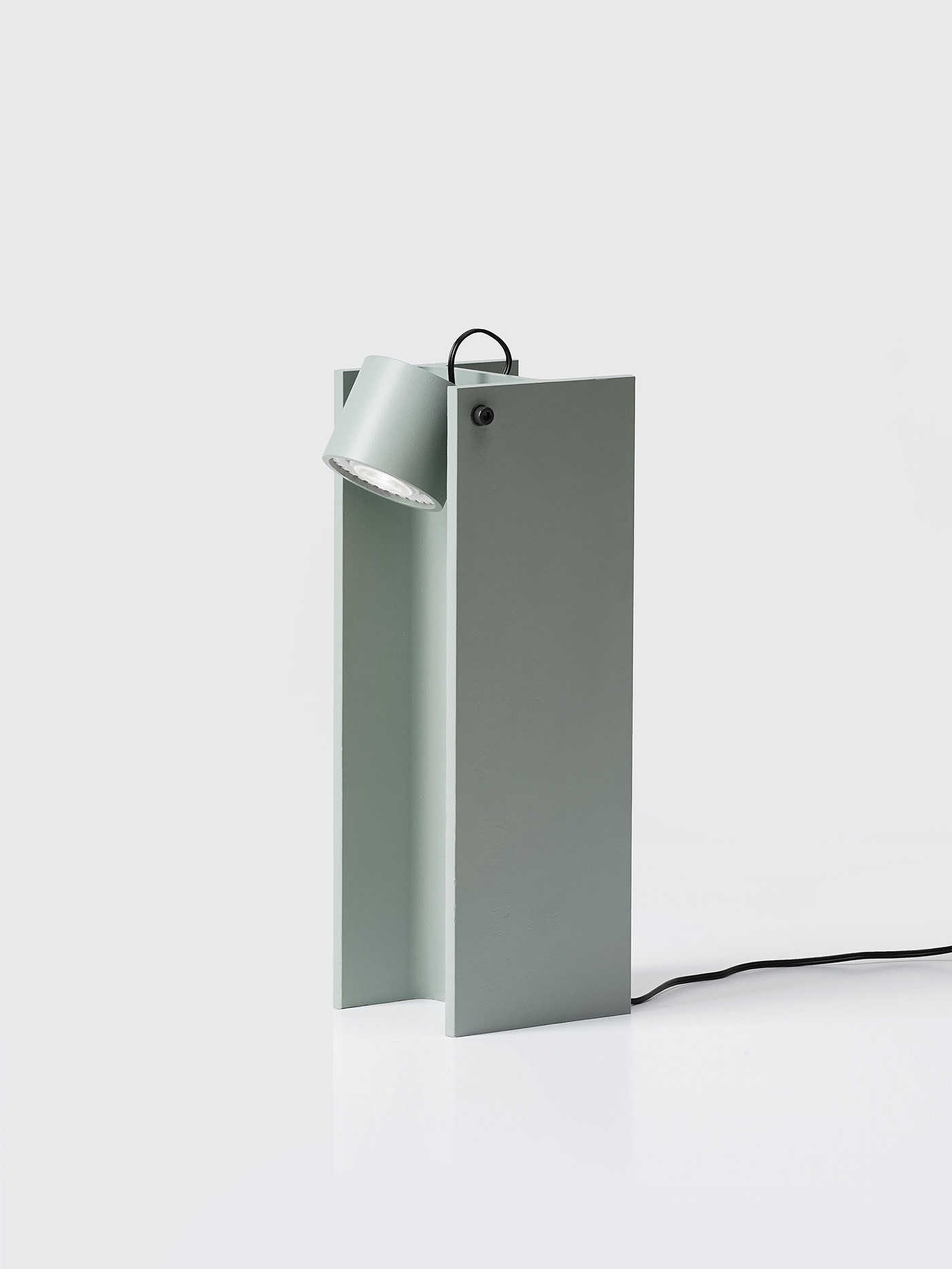 H-beam Lamp Series by SF-SO — The H-beam Lamp Series presents a compact table variant in sage-colored sheet metal, featuring a cylindrical rotating lampshade mounted at the apex of a...