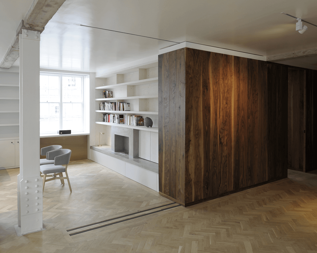 Queens Court by Feilden Fowles — A rectilinear timber volume in dark walnut dominates the foreground, its full-height paneling wrapping two sides to create a defined spatial enclosure.
