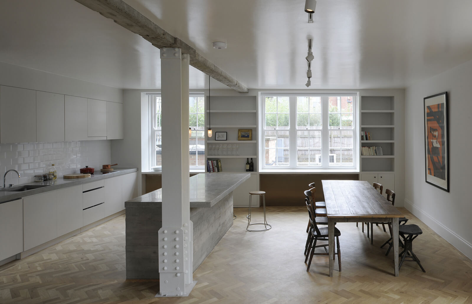Queens Court by Feilden Fowles — A kitchen-dining open plan in a 1930s mansion block apartment, divided by a load-bearing concrete column clad in white-painted metal.