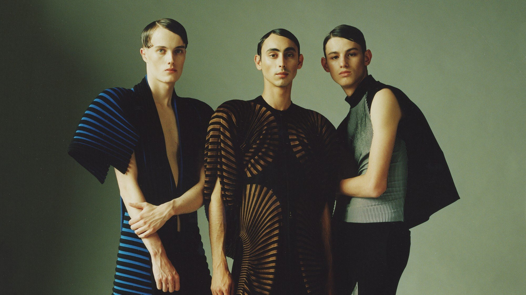 MA Collection by Martin Tual by Martin Taul — Three models positioned against a sage-green backdrop in a symmetrical composition showcase Martin Tual's MA Collection with precision tailoring and...