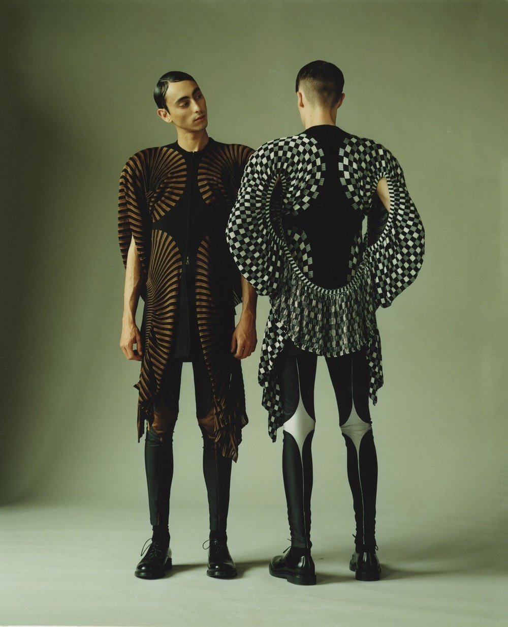 MA Collection by Martin Tual by Martin Taul — Two figures stand in profile against a sage-green backdrop, wearing sculptural knitwear from Martin Tual's MA Collection.