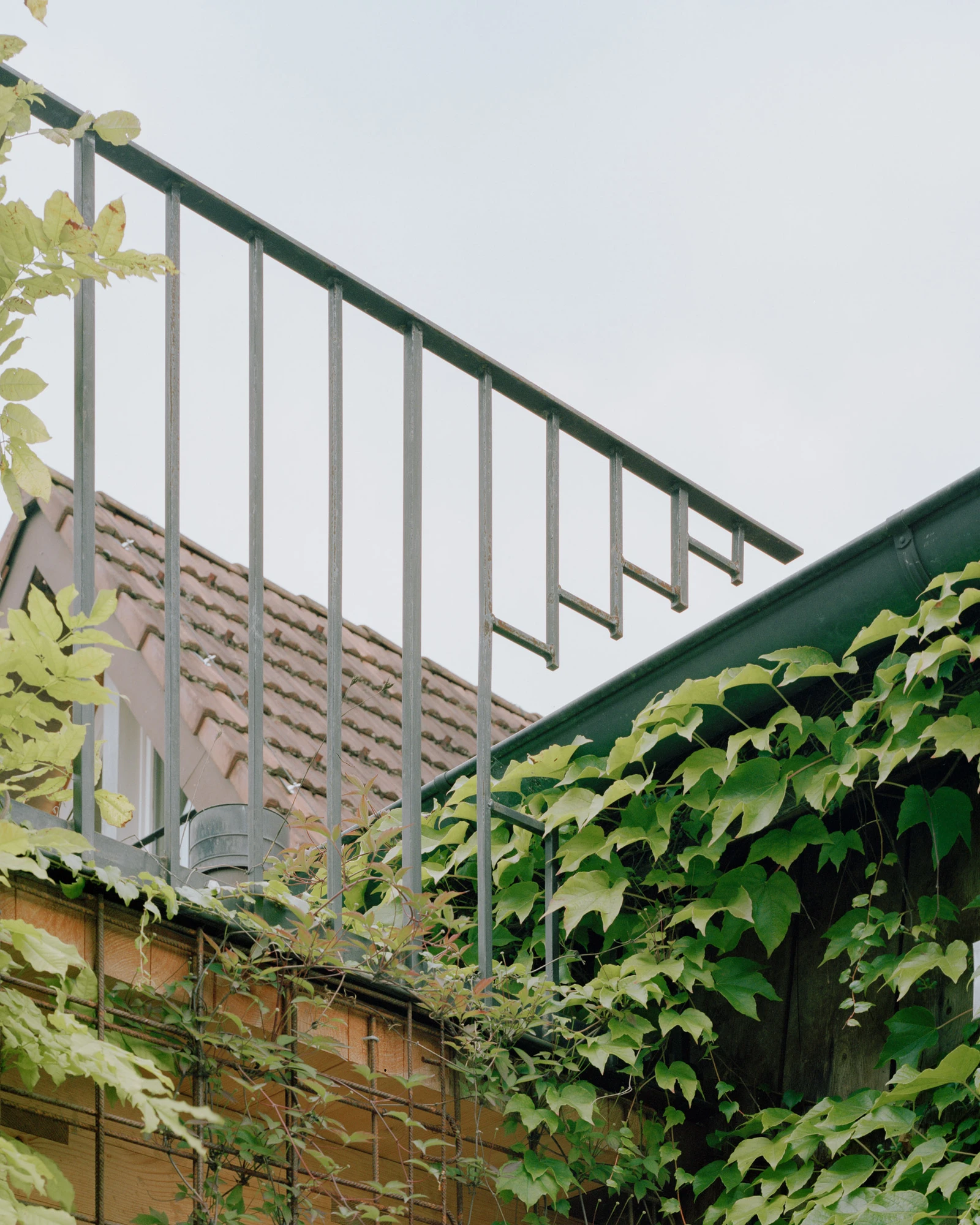 House in Deitingen by studio ou — A metal staircase with vertical steel balusters ascends along a brick facade, its geometric framework casting defined shadows against pale sky.