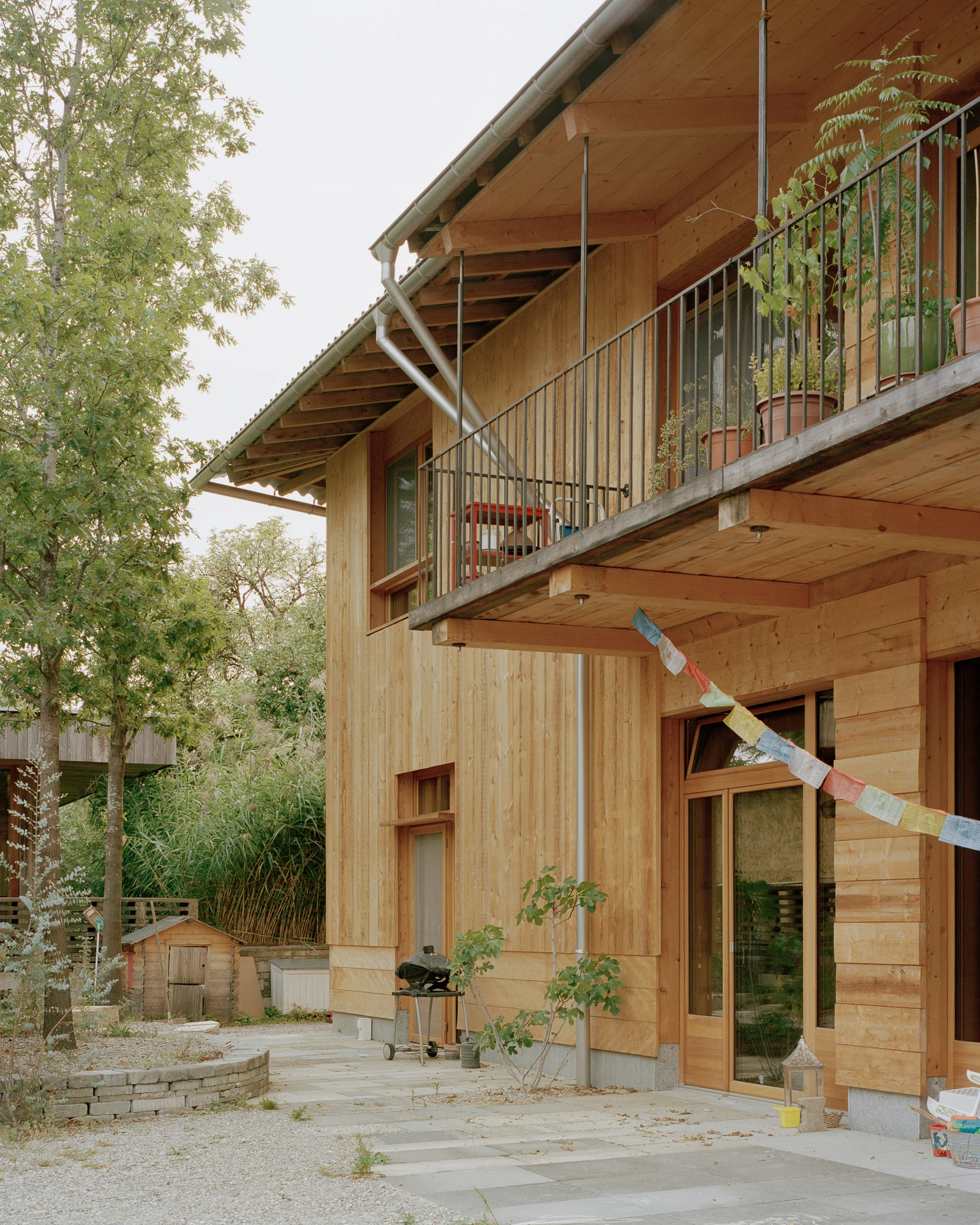 House in Deitingen by studio ou — The south-facing facade of the Deitingen residence displays a two-story timber construction with vertical wood siding in warm honey tones.