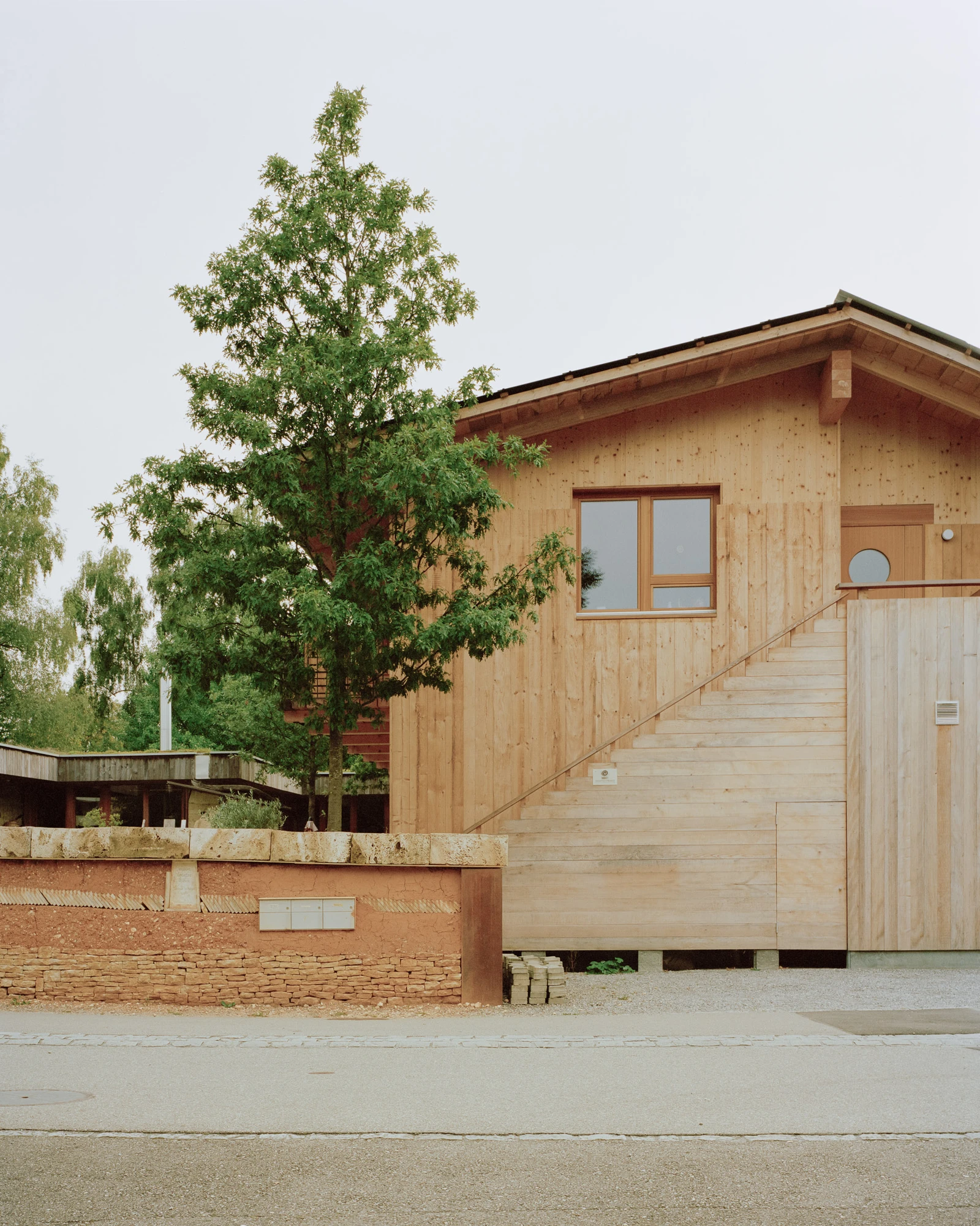 House in Deitingen by studio ou — The timber-clad residential volume sits elevated on a concrete plinth, with a brick retaining wall anchoring the sloped site.