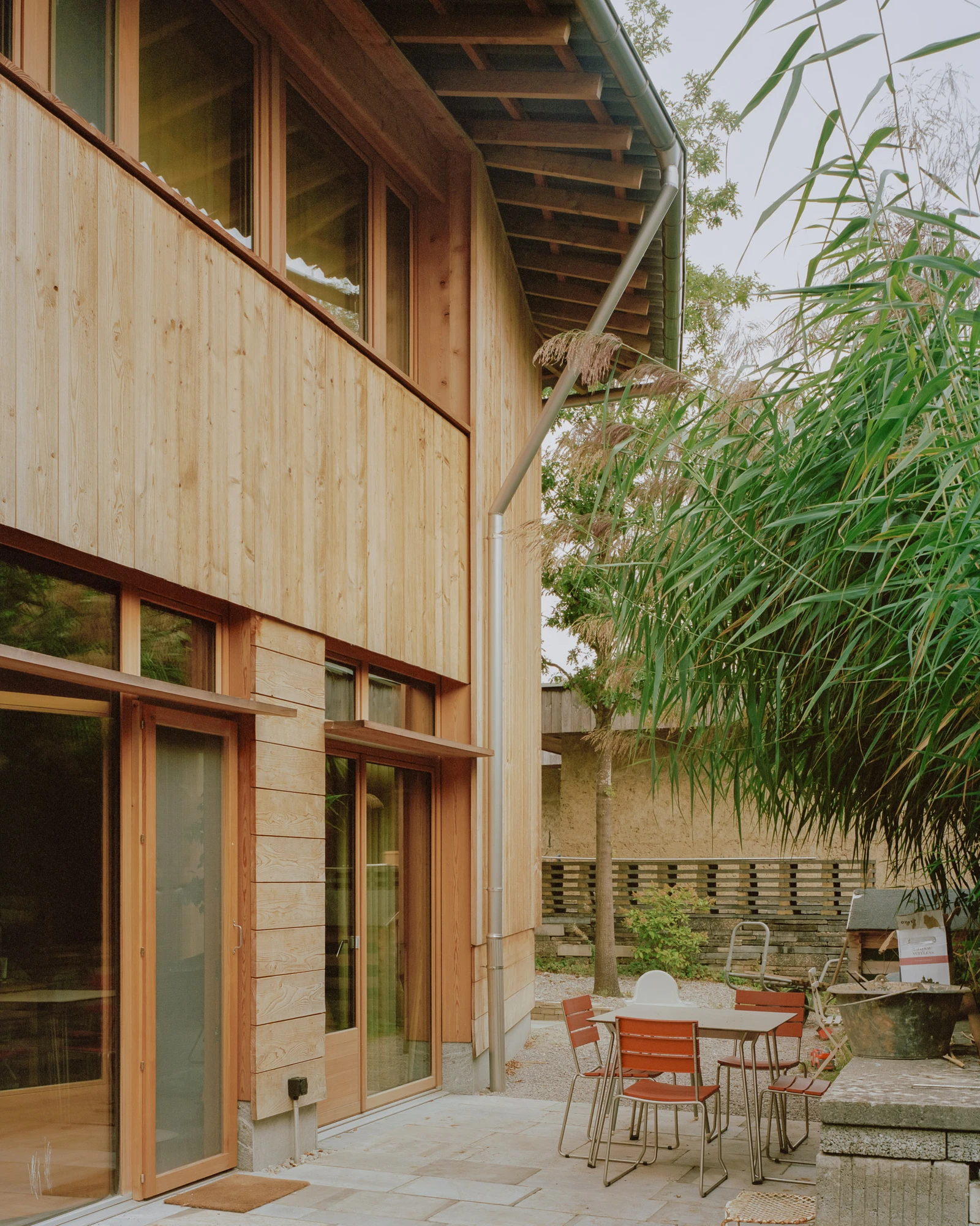 House in Deitingen by studio ou — The courtyard elevation reveals studio ou's material strategy: a timber-clad upper volume in light pine contrasts with a lower stone plinth and rendered wall.