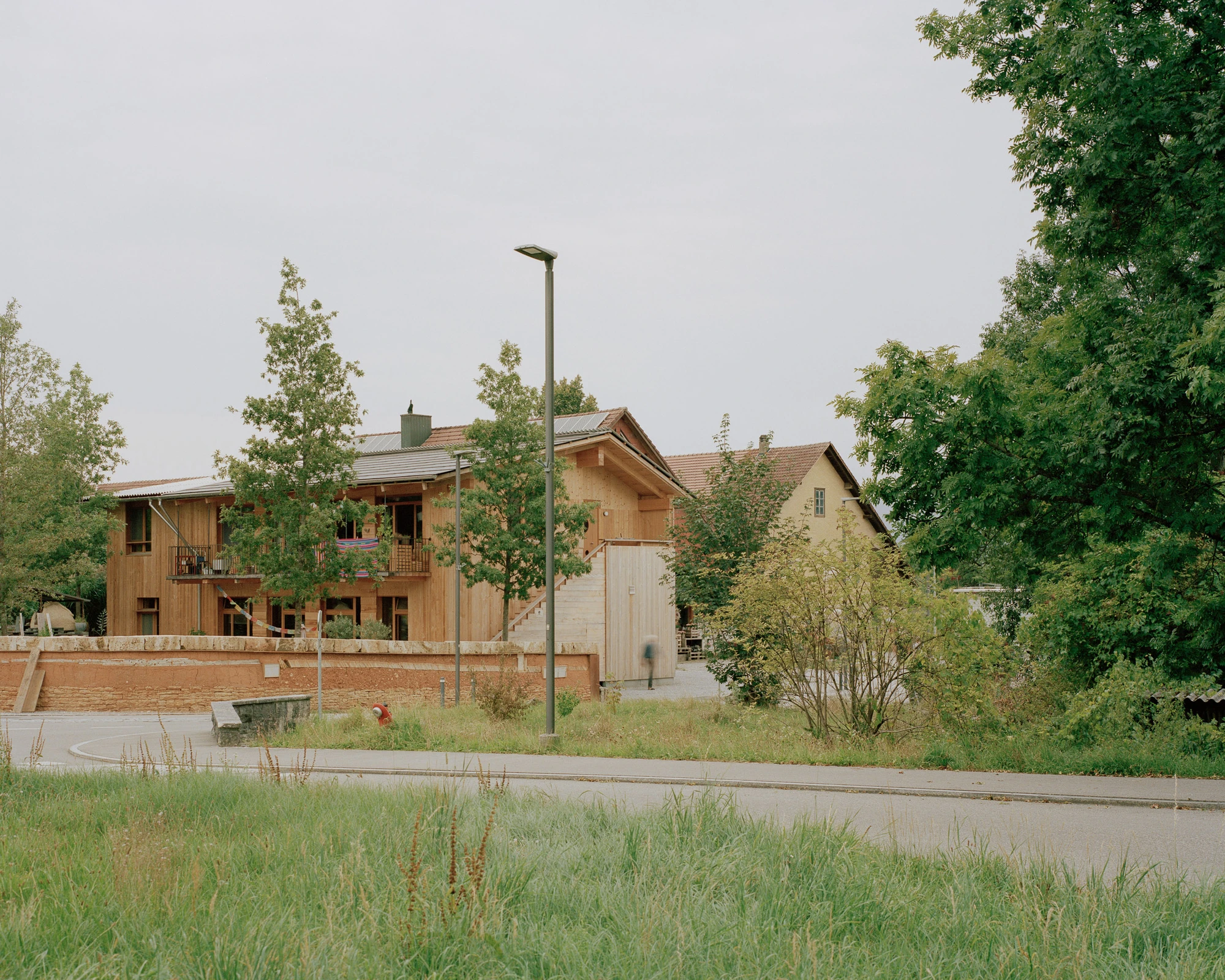 House in Deitingen by studio ou — The timber-clad residential building sits elevated on a brick plinth within the village core, its board-formed wood facade and pitched roof responding to...