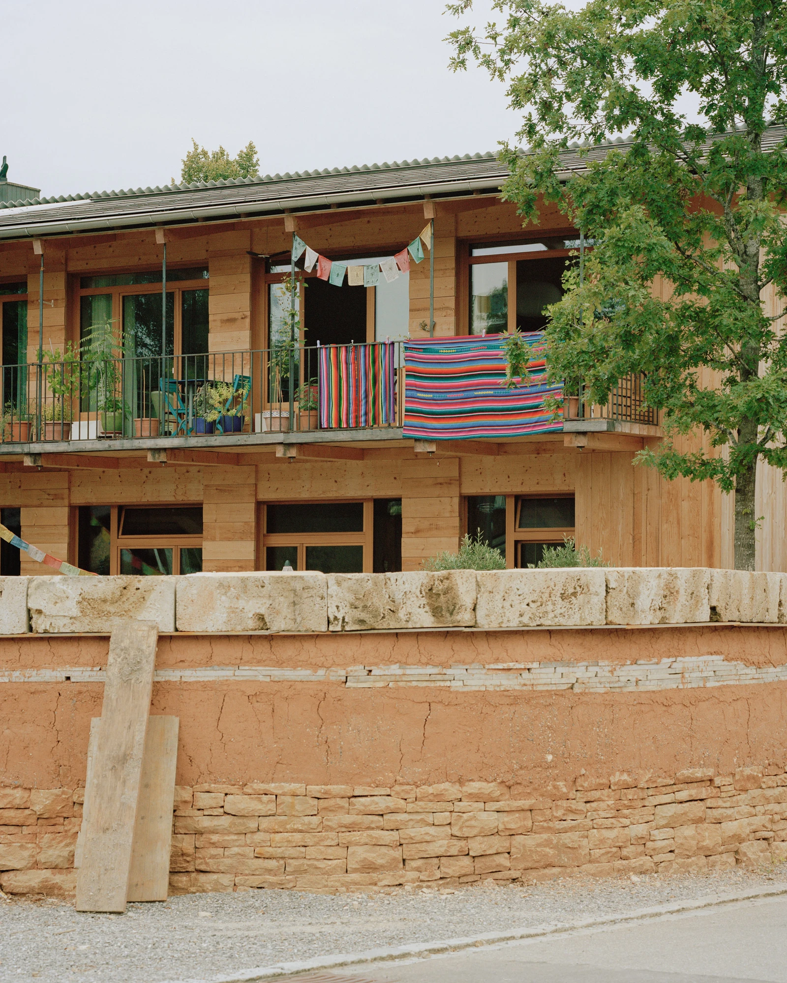 House in Deitingen by studio ou — The upper residential story presents a timber-clad facade with regularly spaced windows and a deep overhang supported by exposed wooden beams.