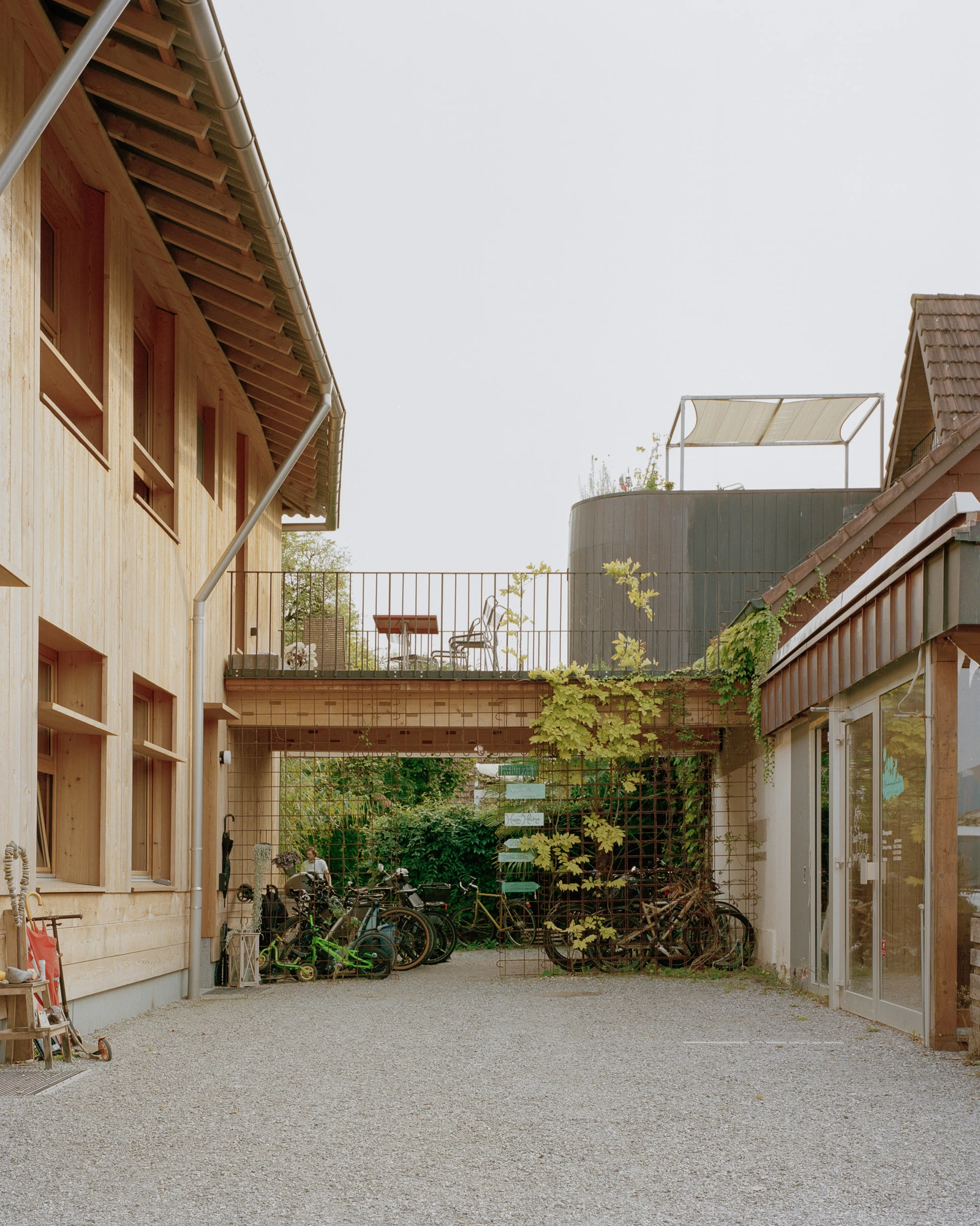 House in Deitingen by studio ou — A gravel courtyard bounded by timber-clad residential structures and brick masonry walls creates an enclosed outdoor space.