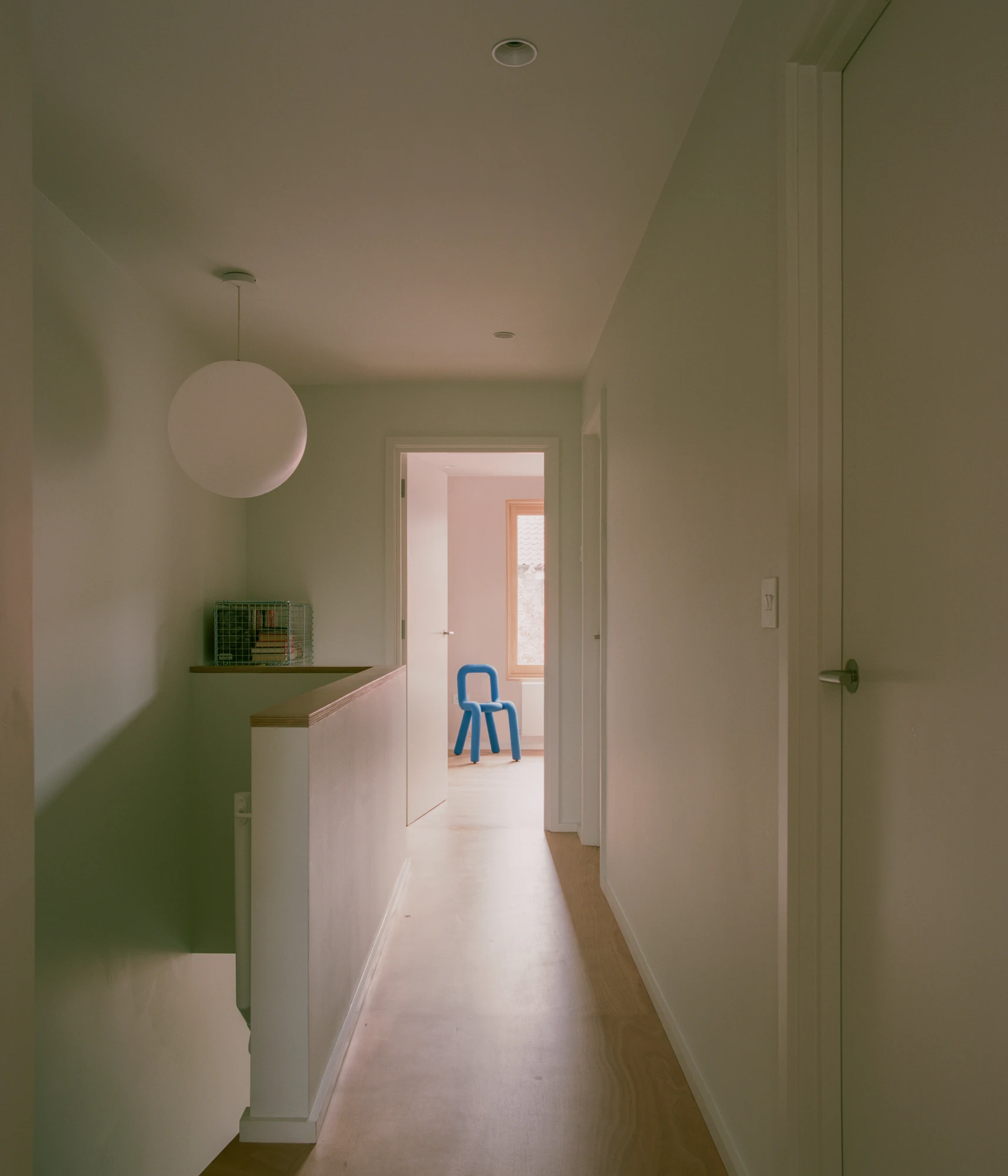 Walthamstow House by PSL — A narrow hallway with white plaster walls and timber flooring extends toward a pink-painted room visible through an open doorway.