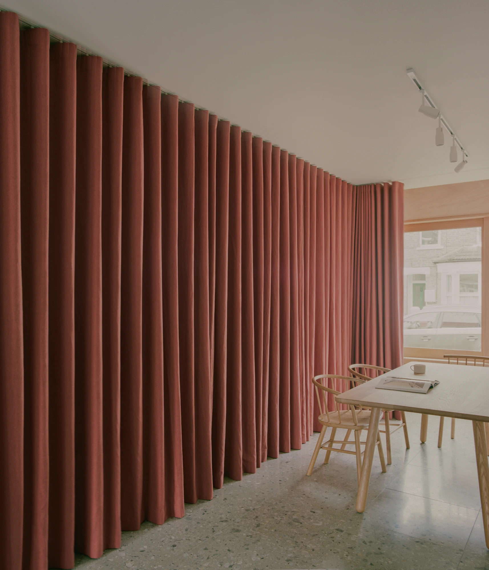 Walthamstow House by PSL — A ground-floor dining space defined by a floor-to-ceiling pleated fabric partition in crimson linen that spans the full wall width, creating spatial...