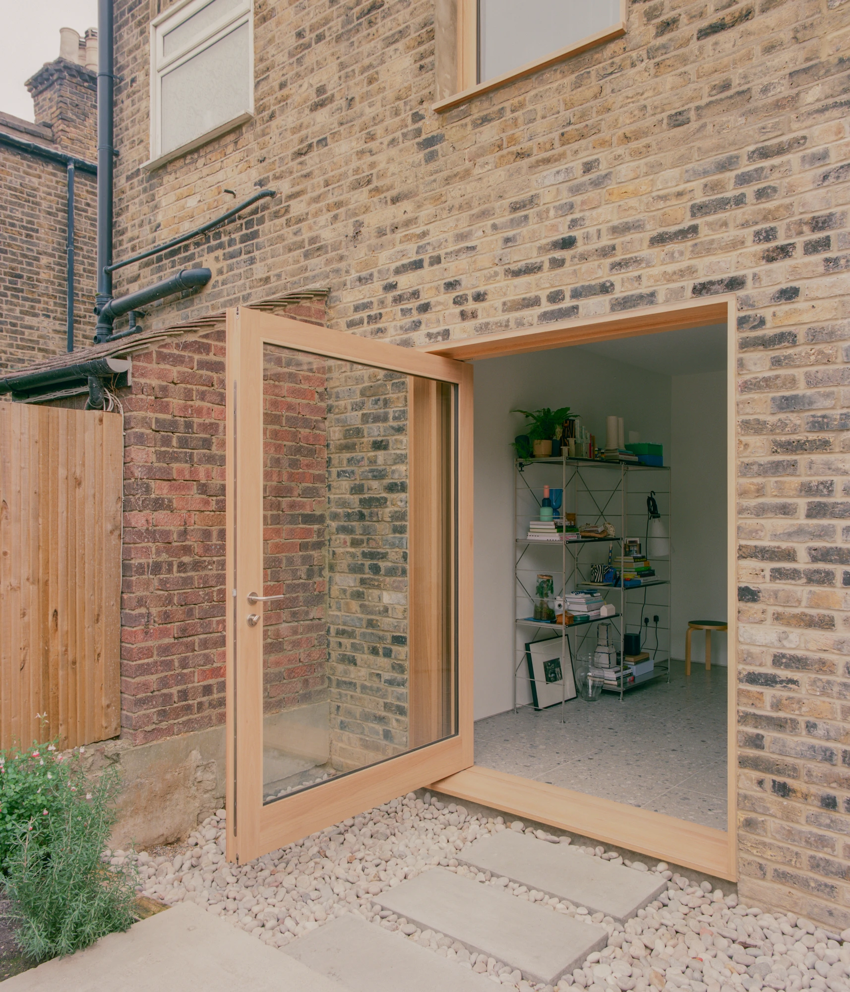 Walthamstow House by PSL — A timber-framed glazed door and window opening onto a garden courtyard, revealing a brick-walled extension interior.