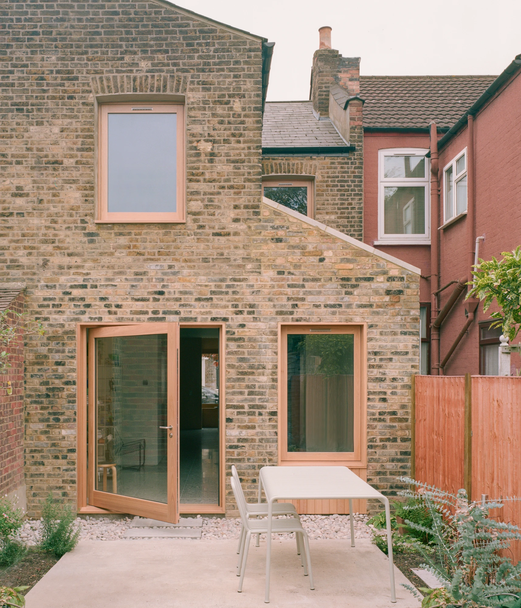 Walthamstow House by PSL — Rear elevation of the Victorian terrace showing the restored ground-floor extension with timber-framed glass doors and window opening onto a gravel courtyard.
