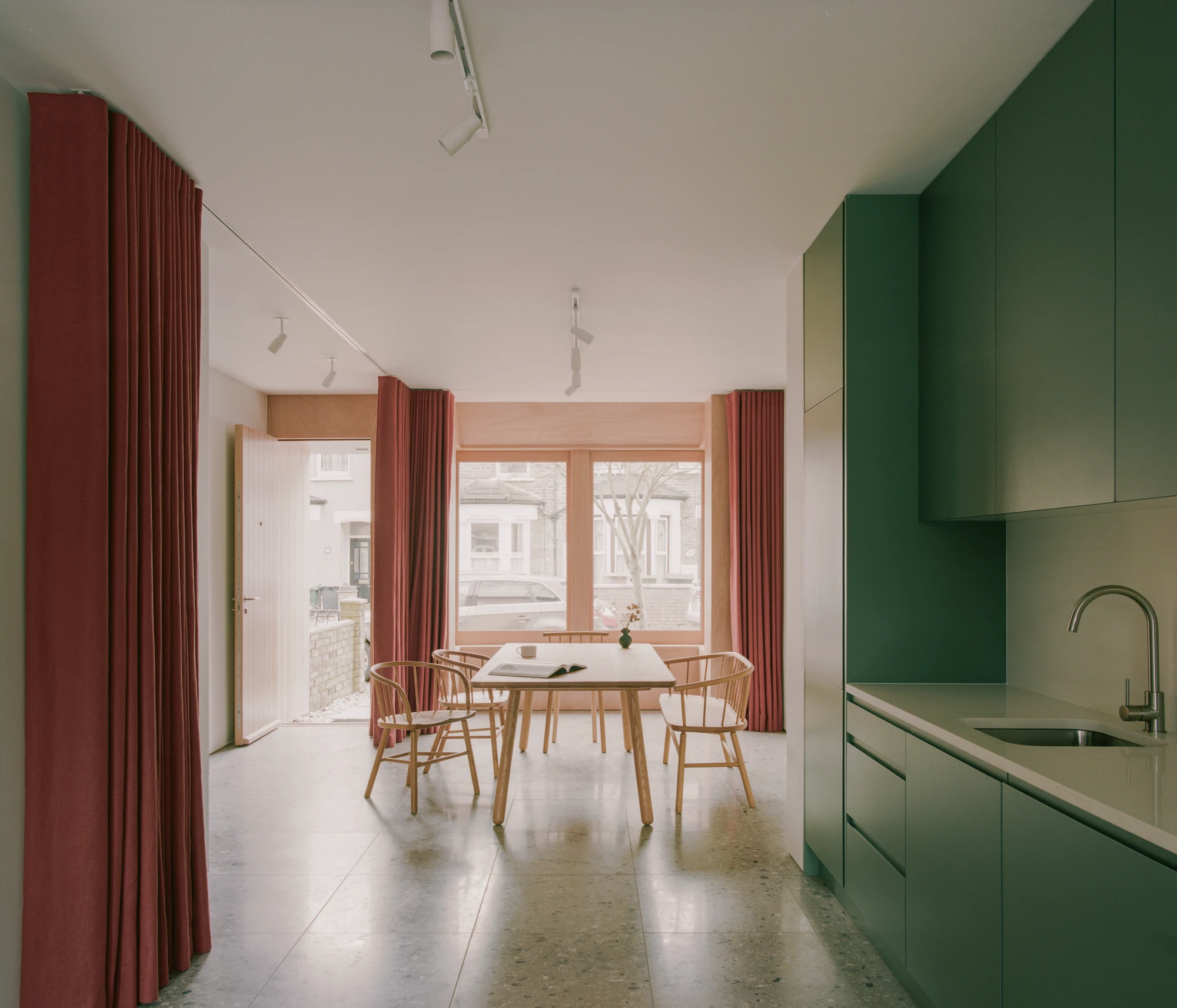 Walthamstow House by PSL — The ground floor dining space frames a wooden table with spindle-back chairs positioned centrally beneath track lighting.