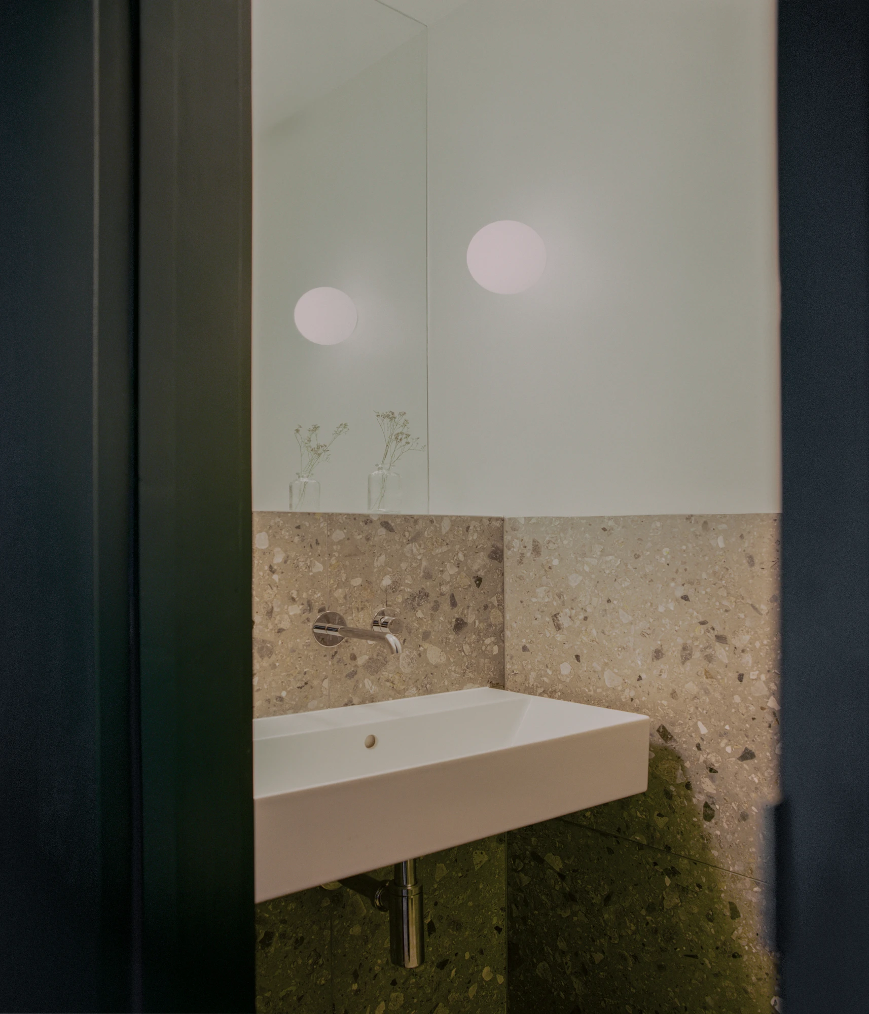 Walthamstow House by PSL — Bathroom detail showing a wall-mounted white rectangular sink positioned against travertine cladding that wraps the lower half of the wall.