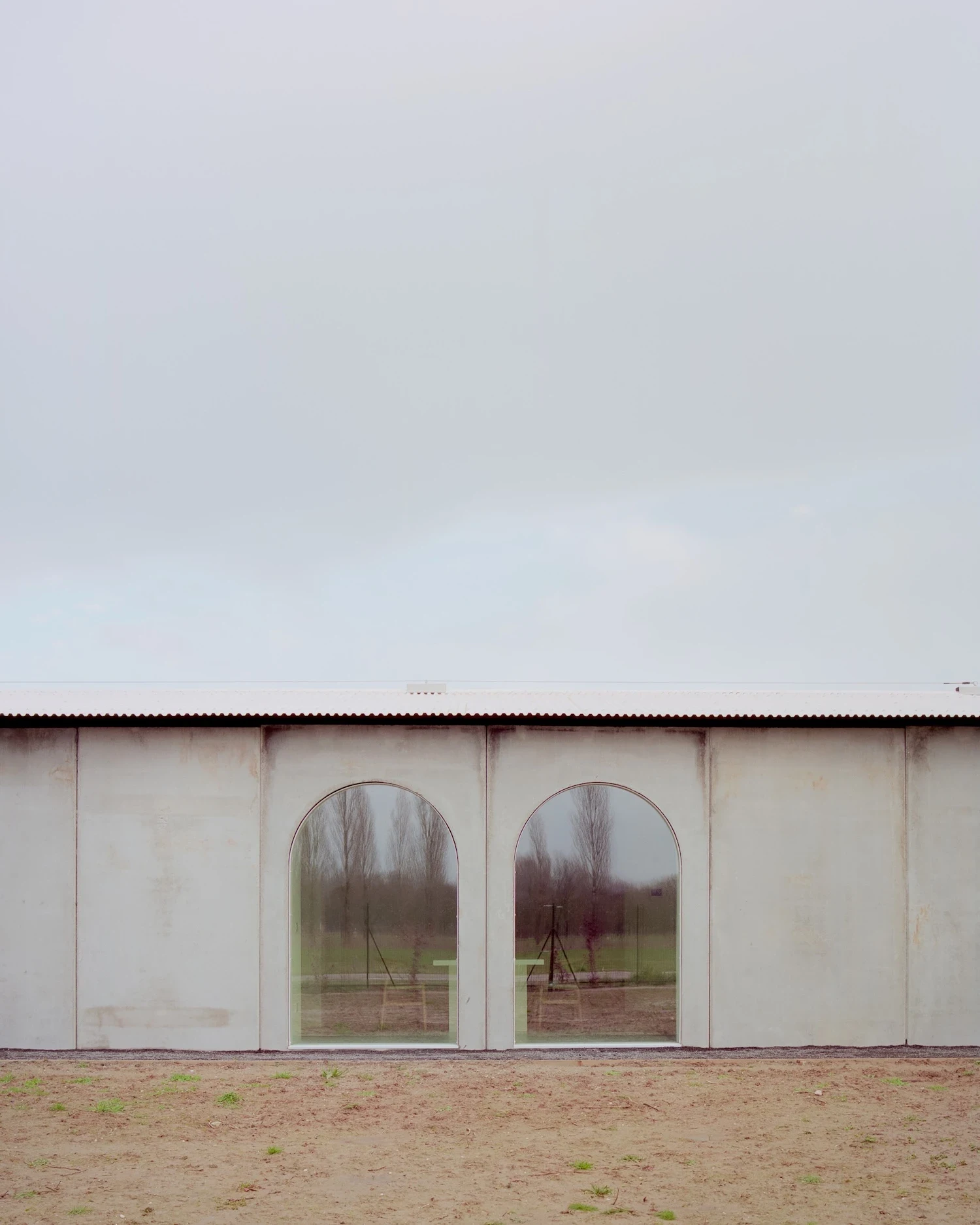 Casa GA by Archiplan Studio — Two arched windows punctuate the rendered concrete facade of Casa GA, their generous proportions framing the flat agricultural landscape beyond.