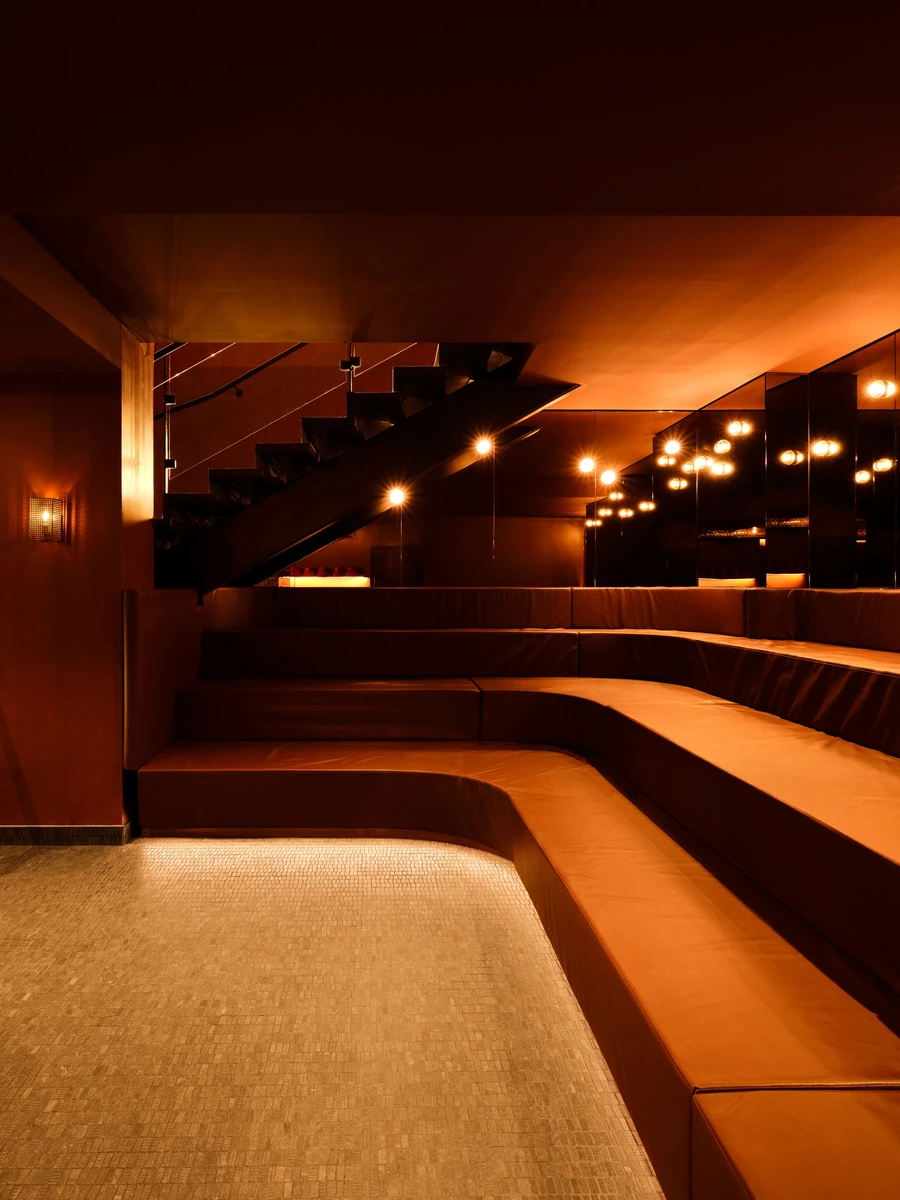 Sant Roch Sauna by Futurstudio — A tiered seating chamber lined in terracotta-hued material descends into darkness, each step backlit by recessed warm-toned lighting.