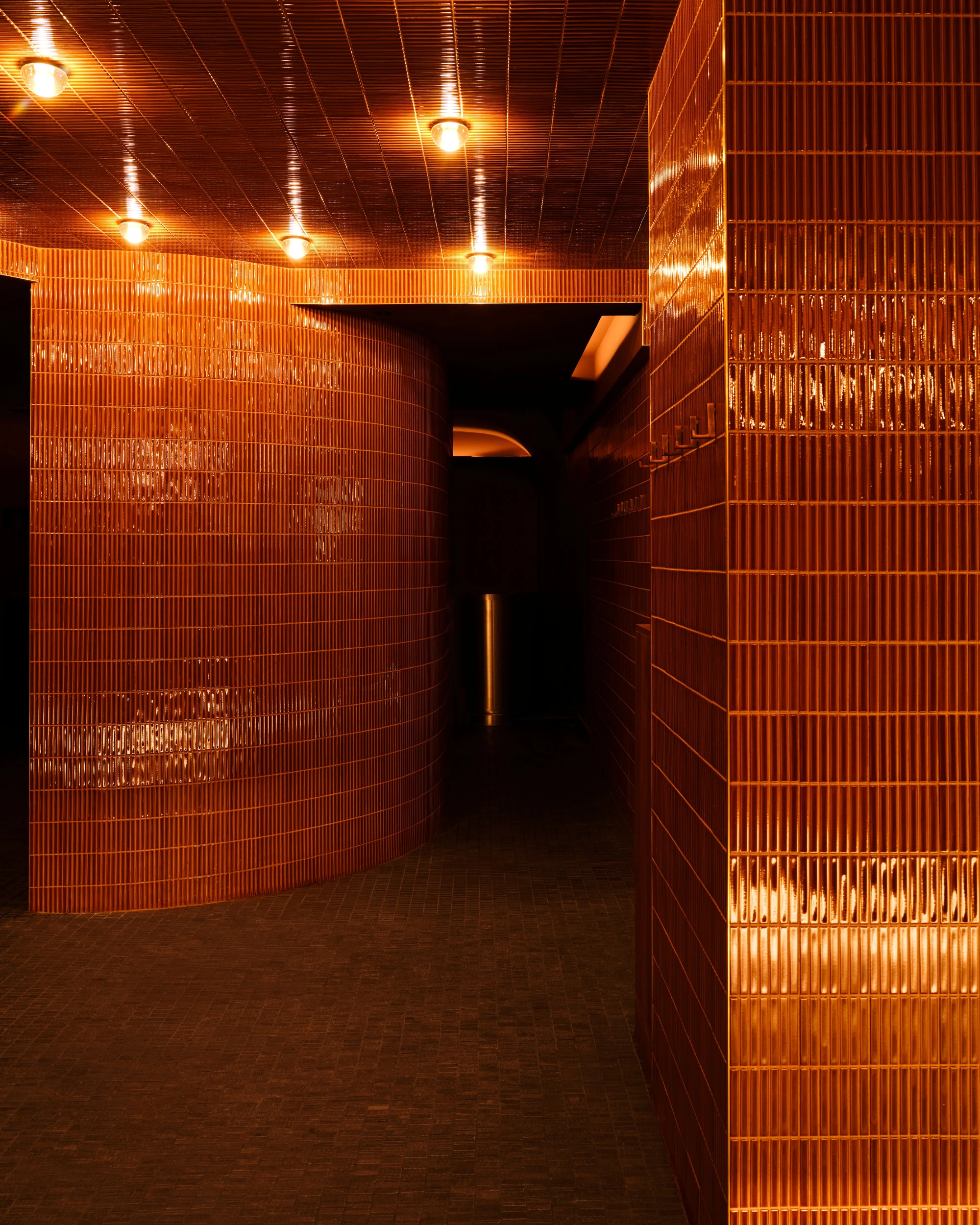 Sant Roch Sauna by Futurstudio — A corridor in Sant Roch Sauna lined with terracotta brick walls arranged in a linear relief pattern.