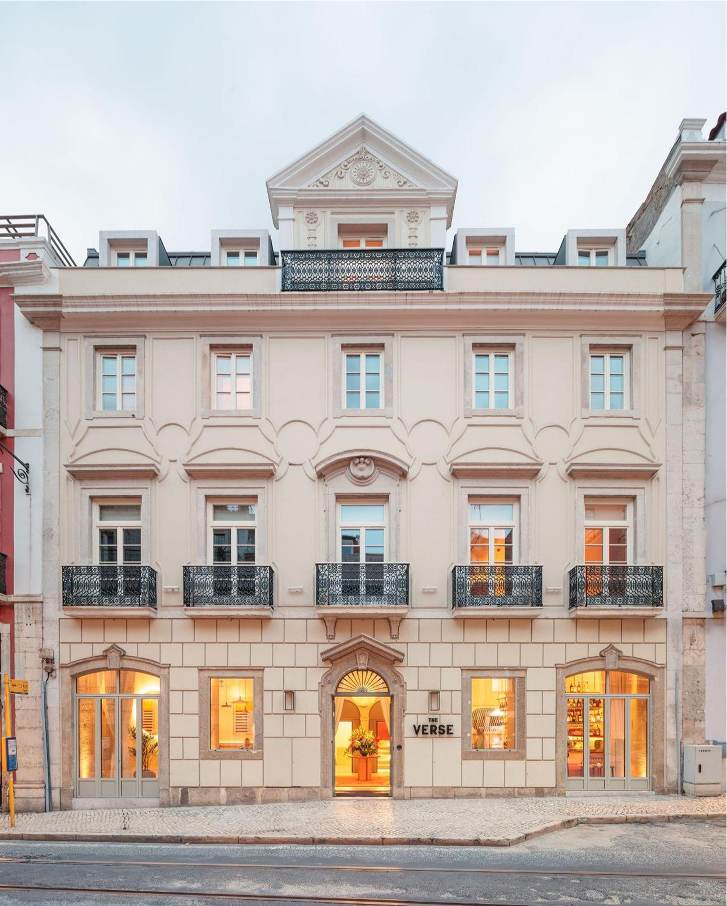 The Verse by João Luís Carrilho da Graça + Studio Astolfi — The street-facing facade of The Verse reveals a rendered stone and plaster exterior in cream and terracotta tones, organized across three storeys with a...