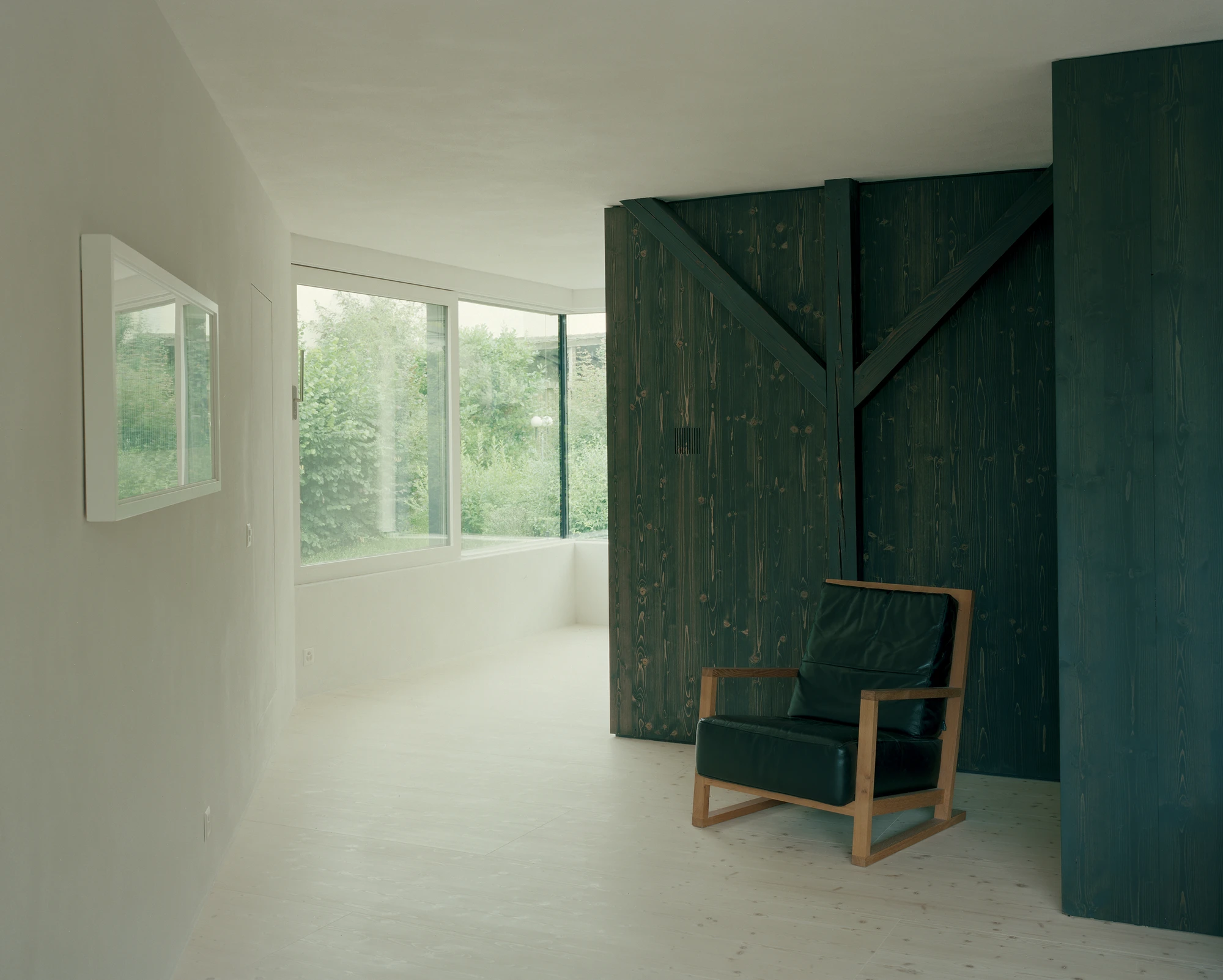 Attic Conversion in Riehen by Raeto Studer Architekten — A monolithic dark green timber-clad volume anchors the white floor plane of this attic conversion.