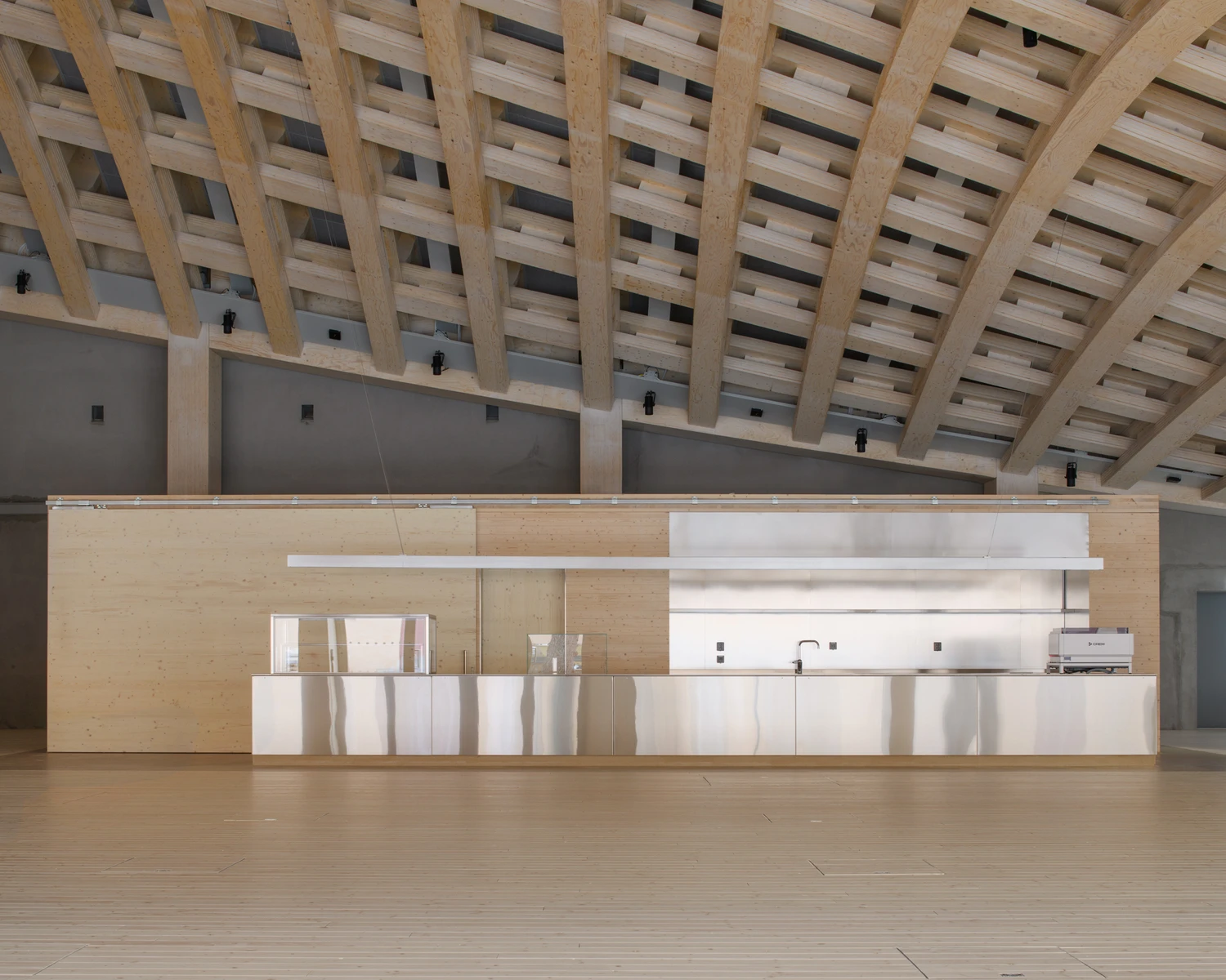 Wisdome Stockholm (National Museum of Science and Technology) by Elding Oscarson — The reception counter occupies the foreground of the vaulted hall, a horizontal datum of plywood and white lacquered surfaces that anchors the spatial...