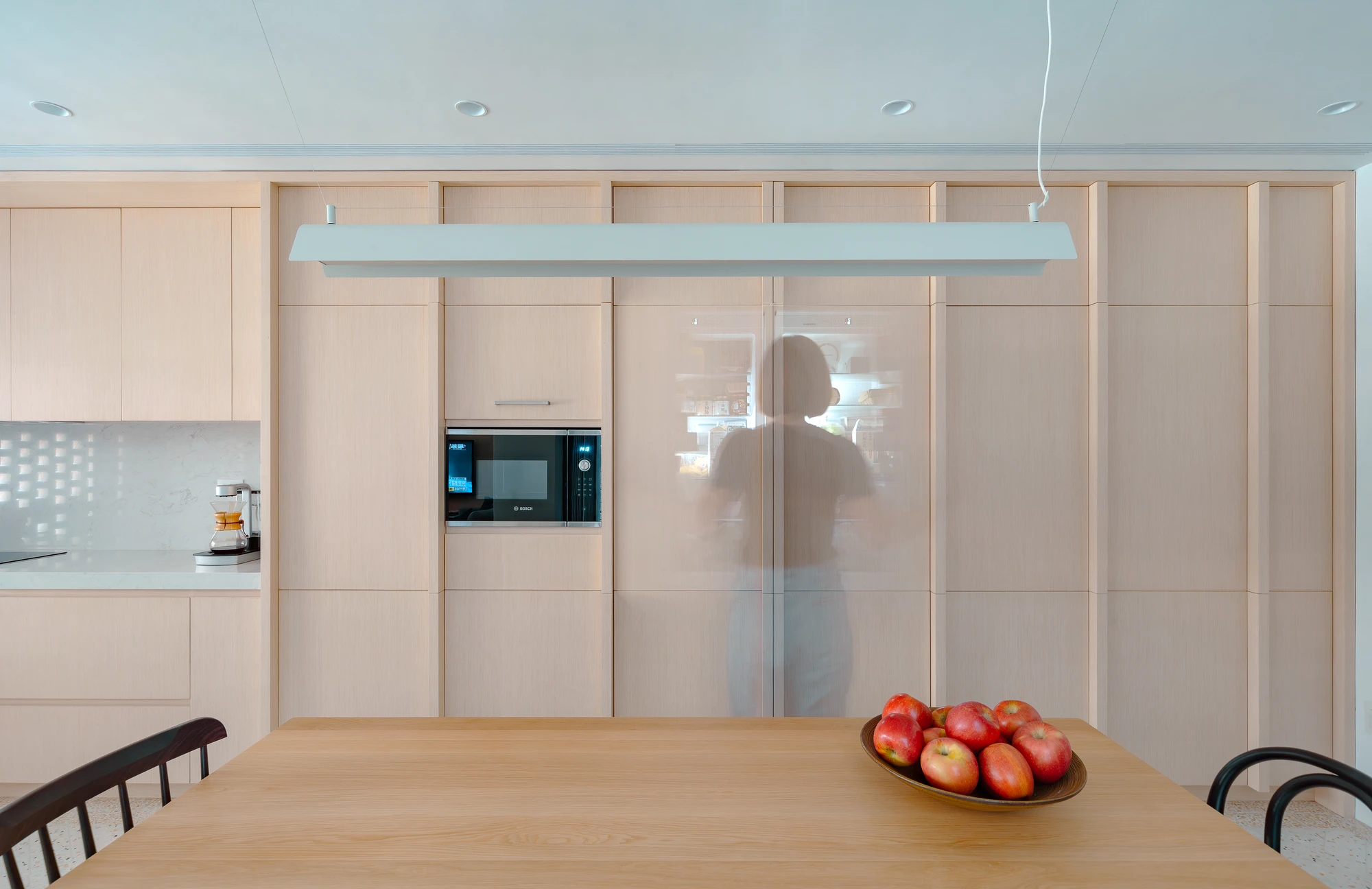 The Veil House by Paperfarm Inc — Interior view of the Veil House kitchen and dining space, framed by the perforated clay-brick facade visible through floor-to-ceiling glazing.