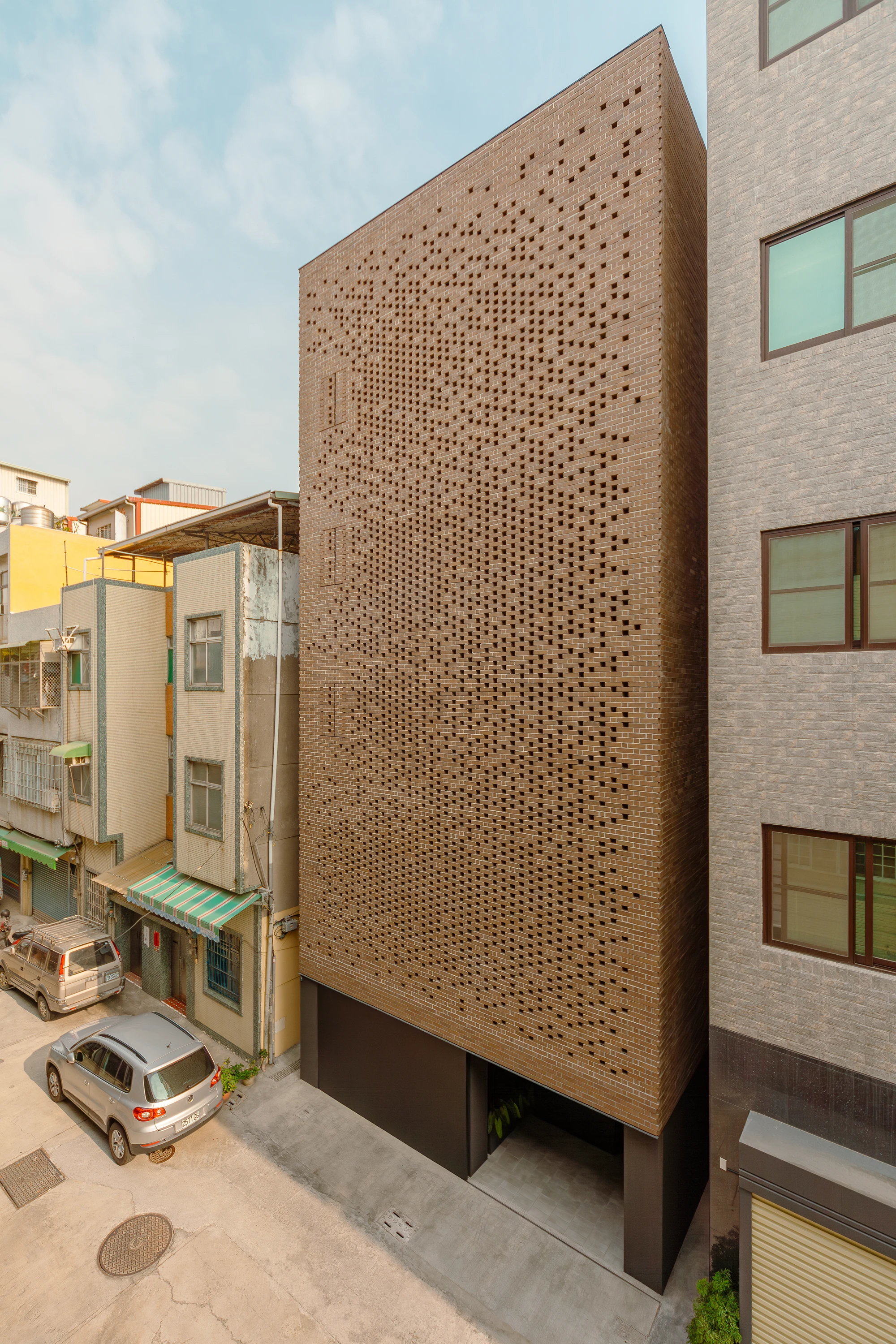 The Veil House by Paperfarm Inc — The Veil House's perforated clay-brick facade dominates this street-level view, its thousands of rectangular voids arranged in a carefully calibrated...