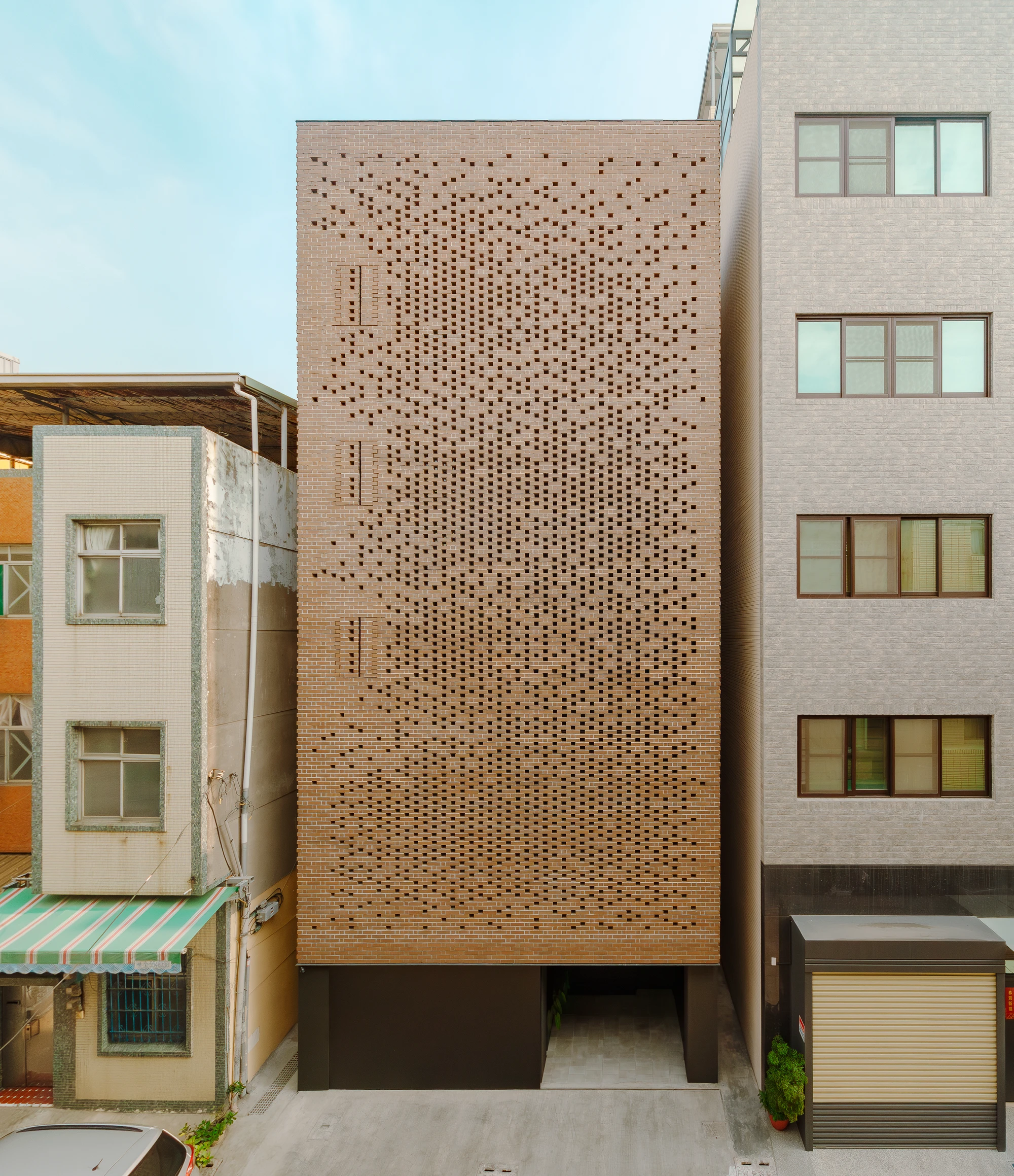 The Veil House by Paperfarm Inc — The Veil House presents a perforated clay-brick facade composed of thousands of small rectangular voids arranged in a gradient pattern that intensifies...