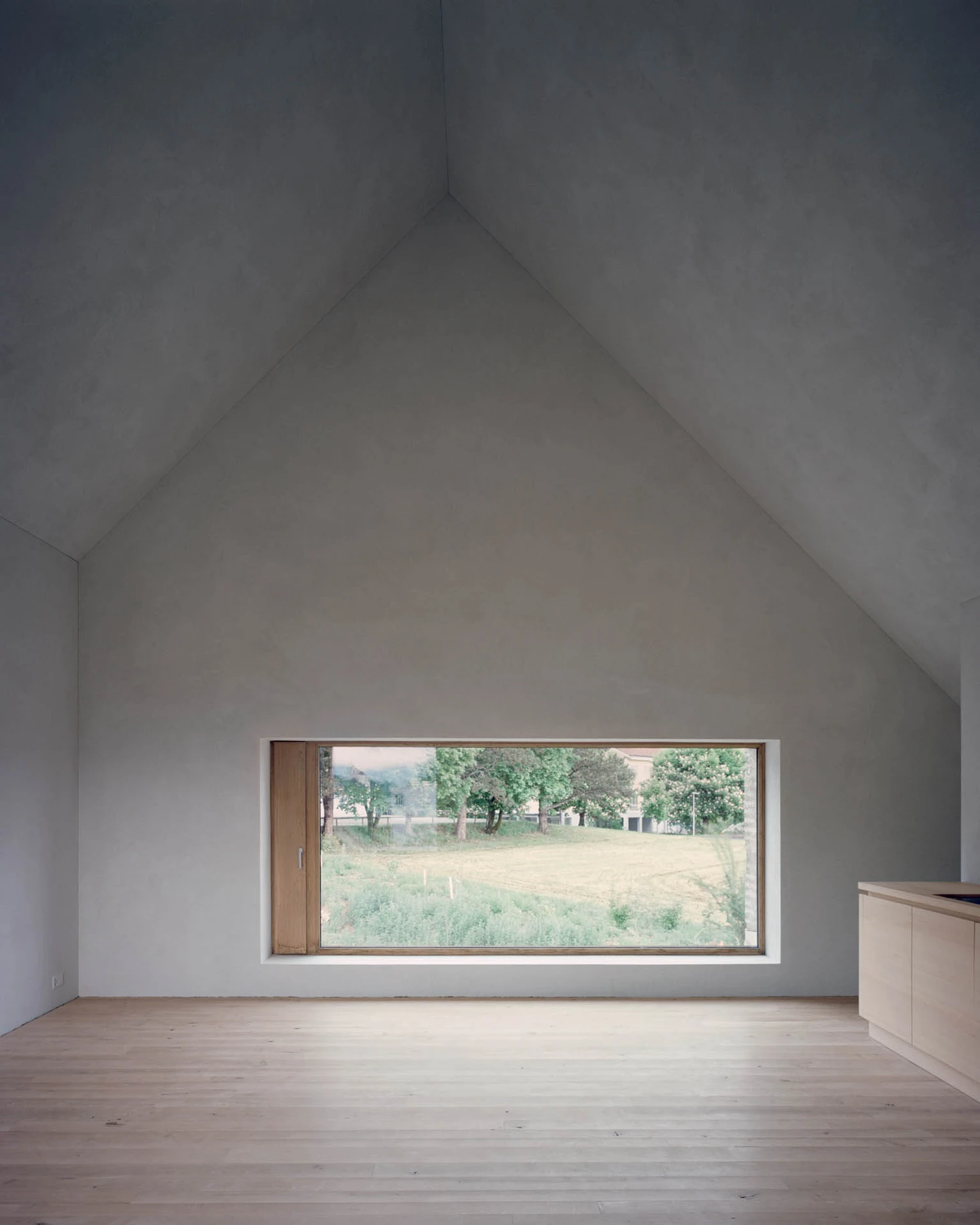 The Gässli5 by allen + crippa architektur — A timber-framed interior beneath a steeply pitched gabled roof, floored in light pine and rendered in white plaster.