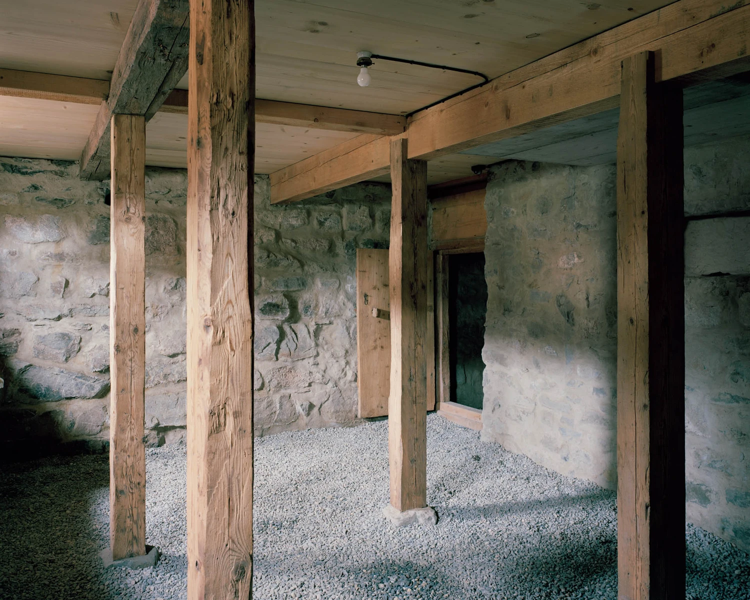 The Gässli5 by allen + crippa architektur — Interior passage beneath a timber-framed structure revealing post-and-beam construction with salvaged wooden columns supporting the ceiling plane.